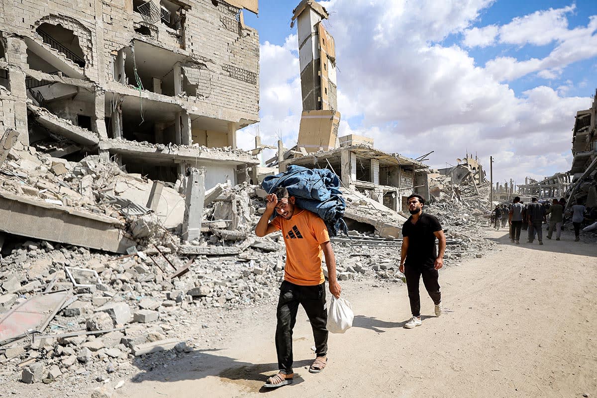 A man carrying a package on his shoulders walks past the rubble of a destroyed building in Khan Younis