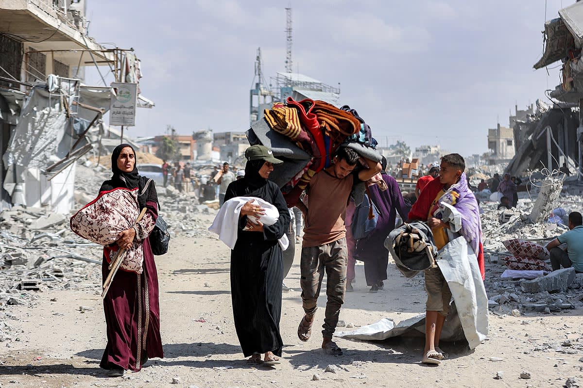 A woman carrying a child speaks with another boy as they walk with other people past the rubble of destroyed buildings in the centre of Khan Younis