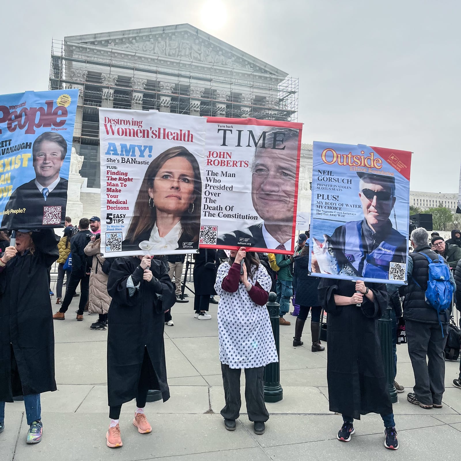 Protestors hold signs with Supreme Court justices faces