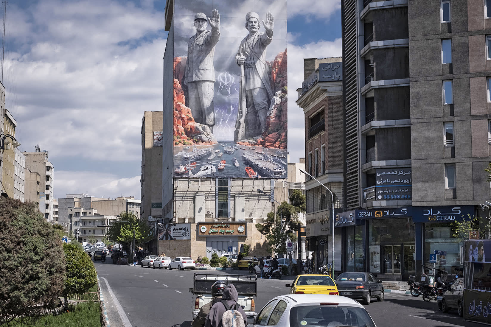 Vehicles drive beneath a billboard picturing a scene related to the Strait of Hormuz on April 9, 2026, in Tehran.