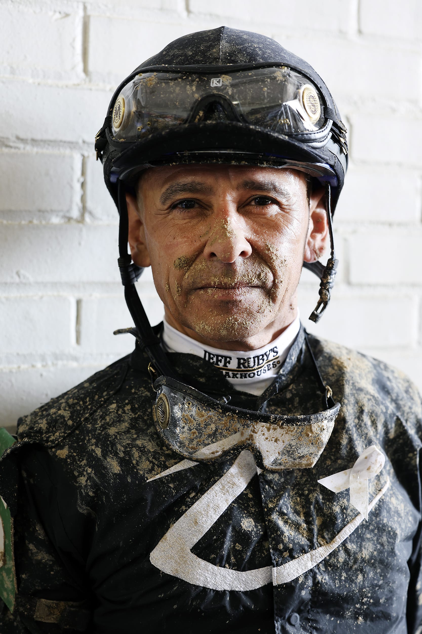 A portrait of jockey Mike Smith wearing a helmet with mud splattered on his face.