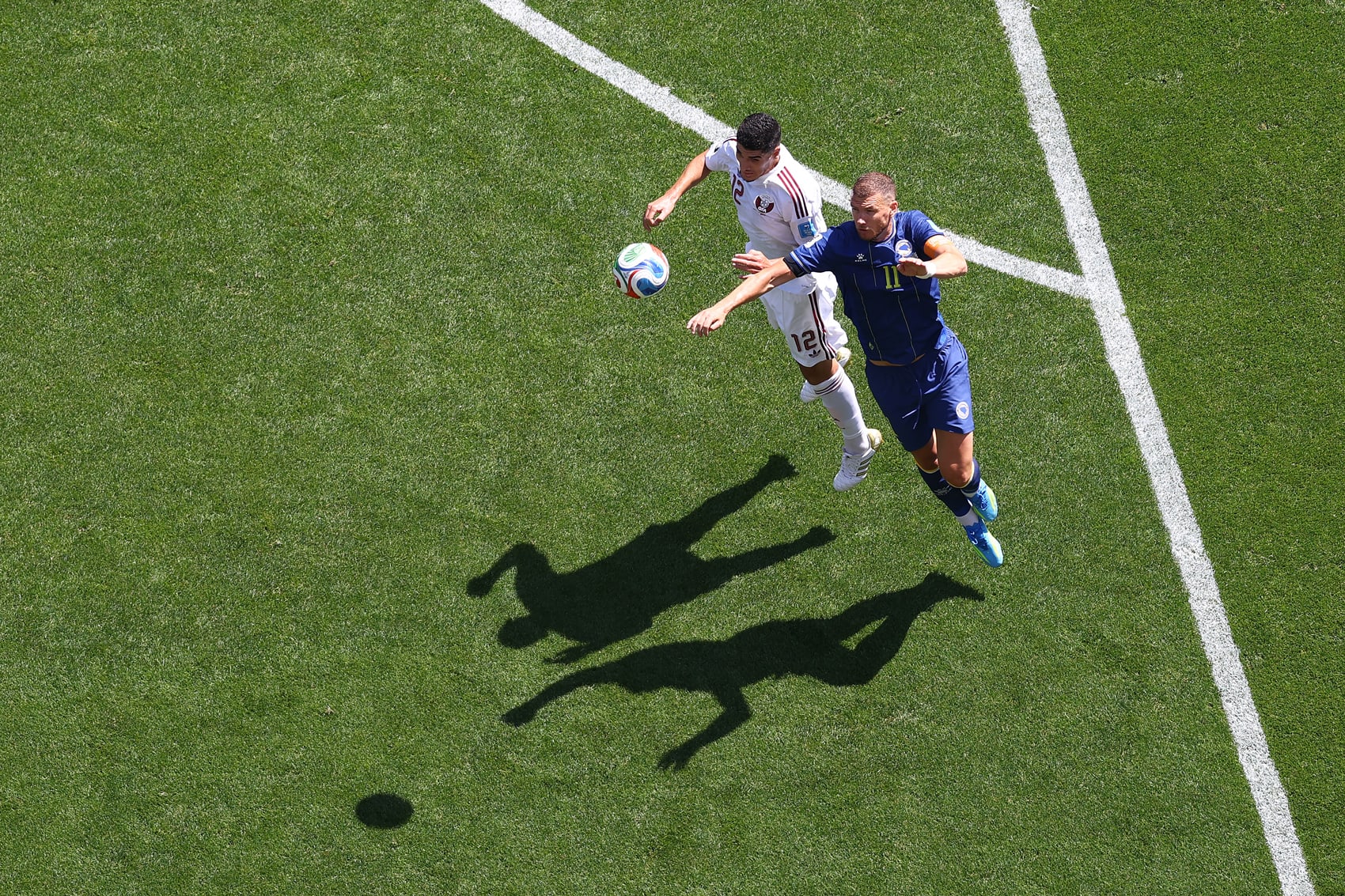 Karim Boudiaf #12 of Qatar competes for a header against Edin Dzeko #11 of Bosnia and Herzegovina