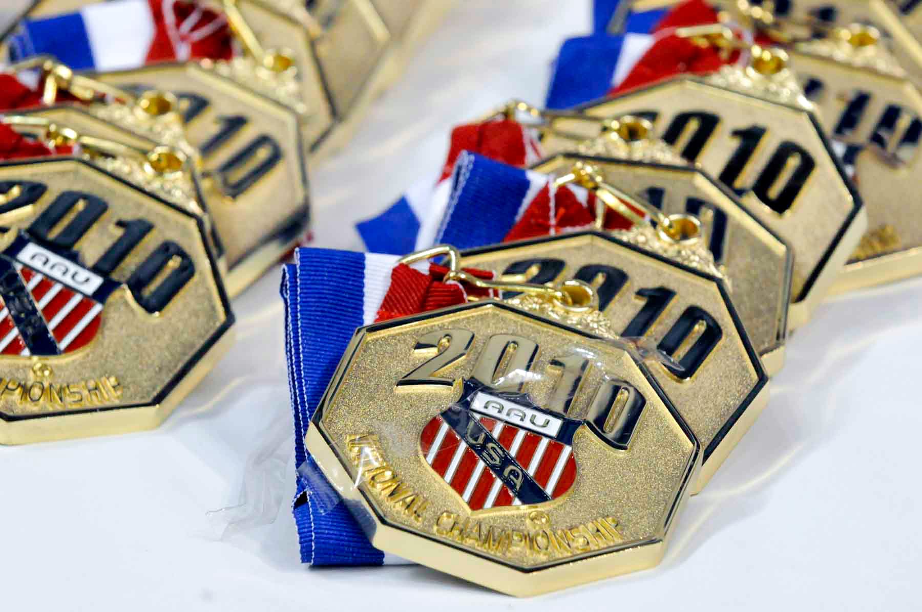 Gold medals with engraved text reading "2010 AAU USA National Championship" with an AAU crest in the center, lined up on a table