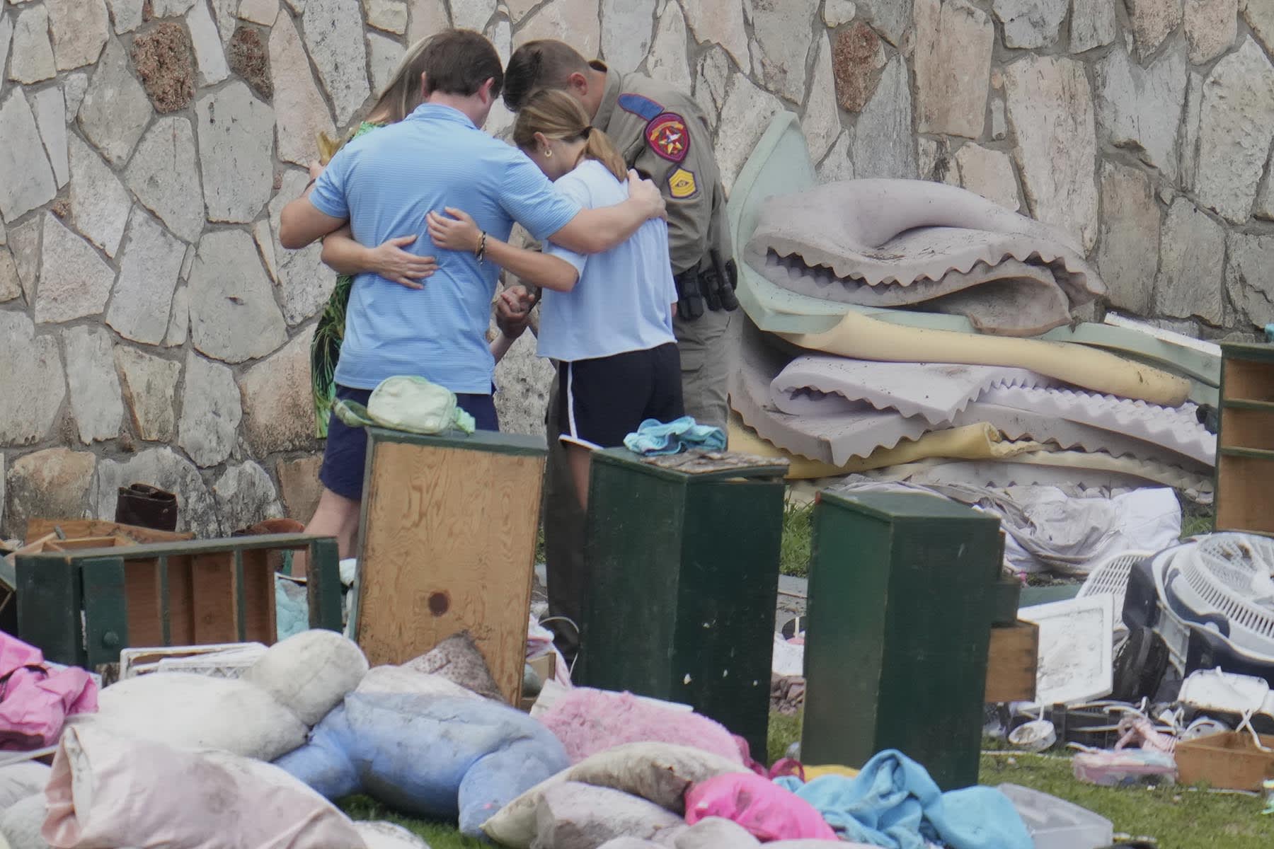 An officer prays with a family as they pick up items at Camp Mystic in Hunt, Texas on Wednesday, July 9, 2025. 