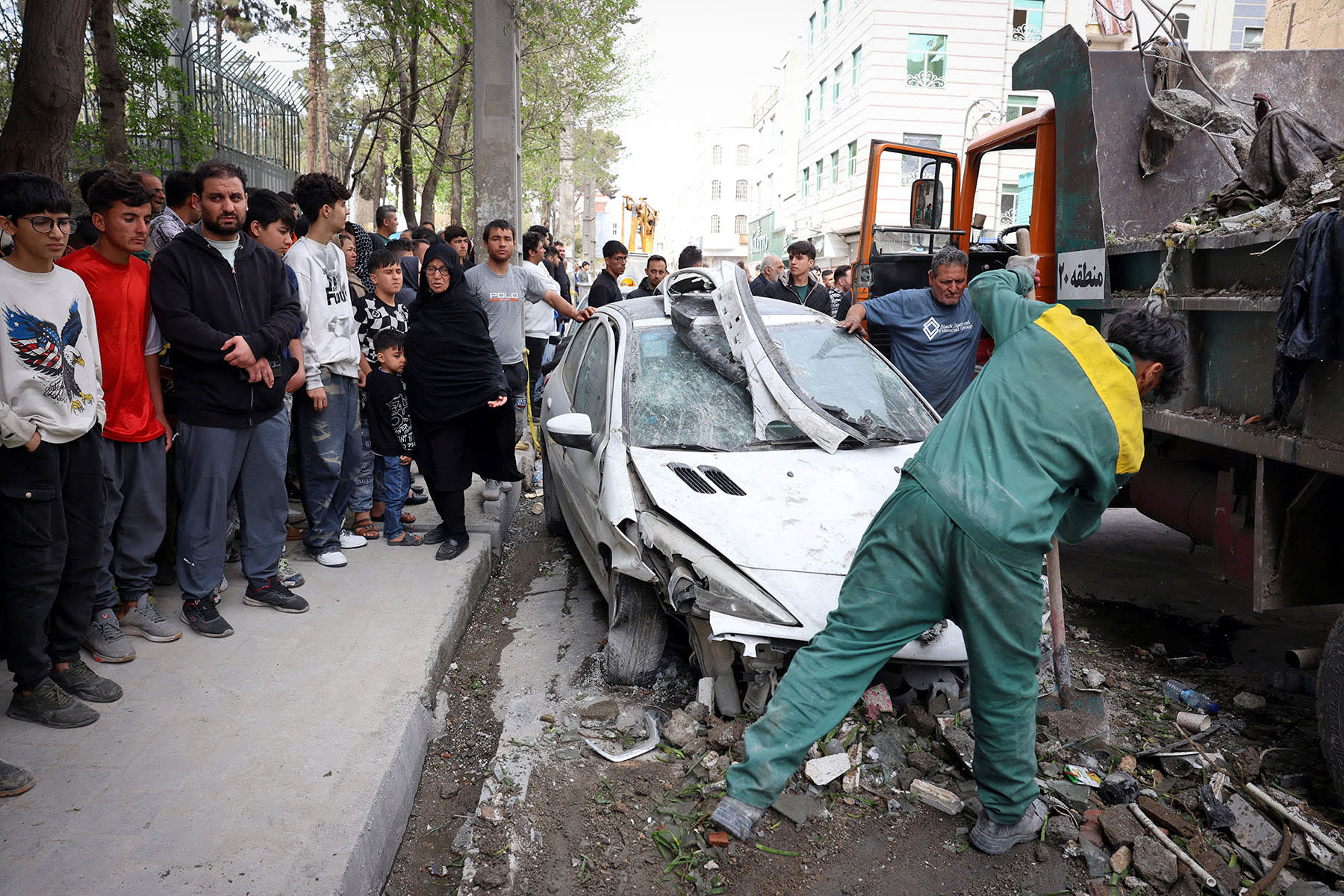Workers remove the wreckage of a car outside a residential building that was targeted in southern Tehran on March 27, 2026.