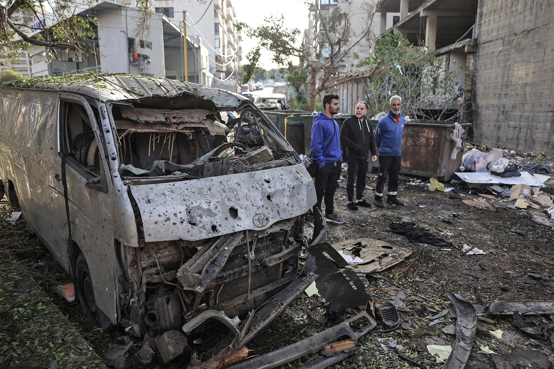 Men look at the damage next to the wreckage of a vehicle at the site of an Israeli strike in Beirut on April 1, 2026. 