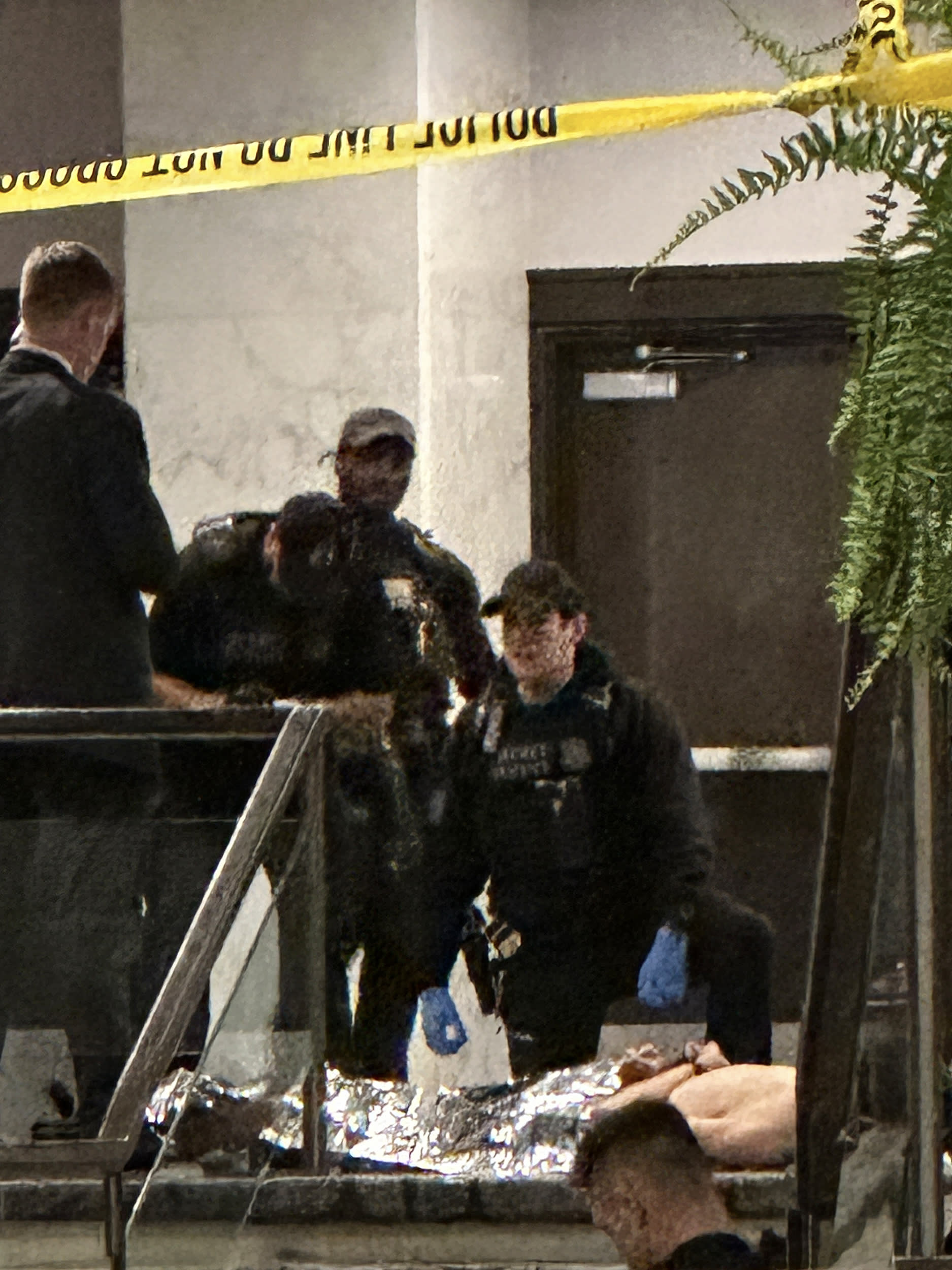 A grainy photo of a shirtless man with his hands cuffed behind his back lying on the floor surrounded by law enforcement officers.