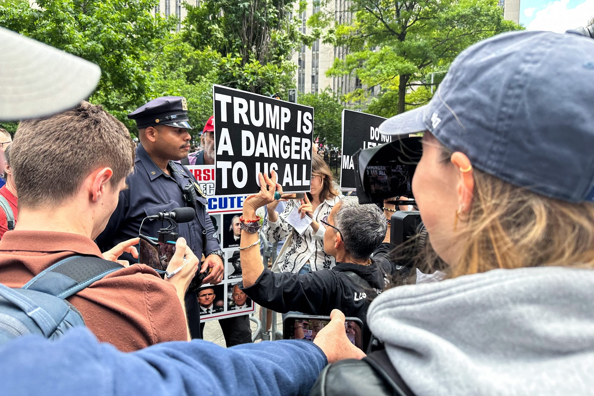 Protestors gather outside, a sign reads "Trump Is A Danger To Us All"