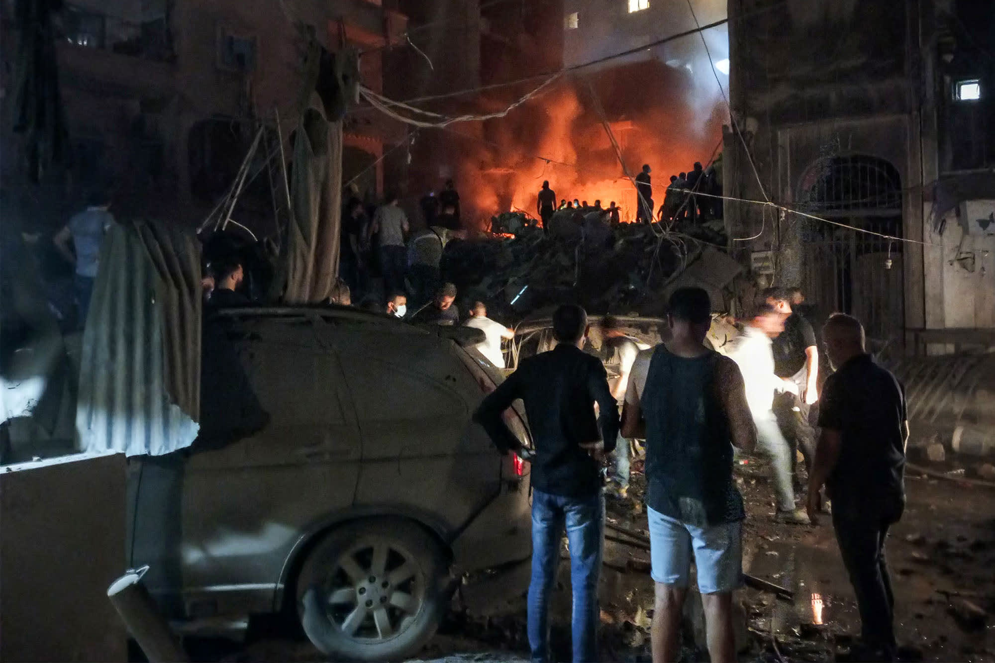 Lebanese civil defense members and others look at the site of an Israeli airstrike on the Basta neighborhood of Beirut