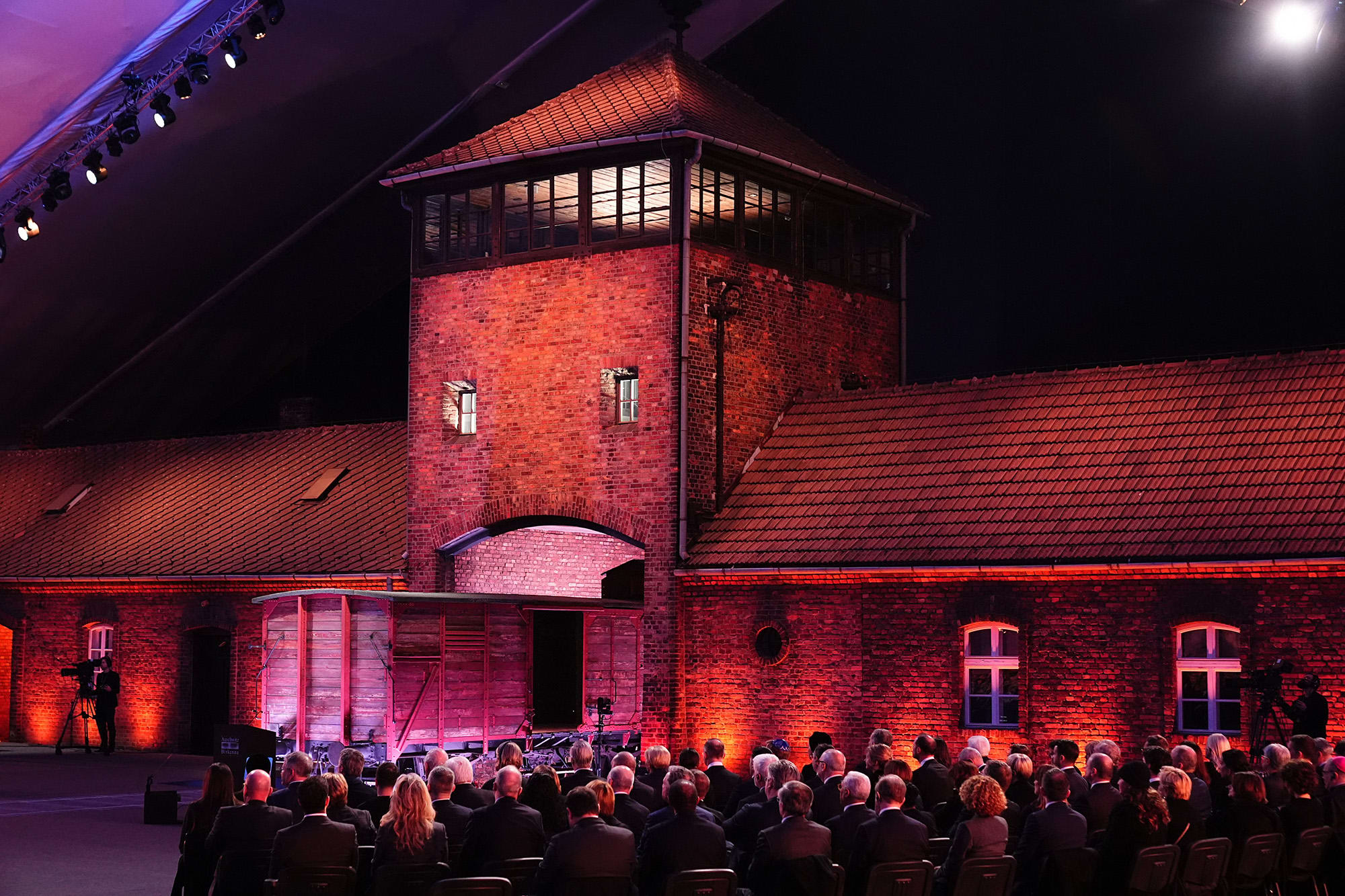 Guests sit in front of the main gate of the Auschwitz-Birkenau camp