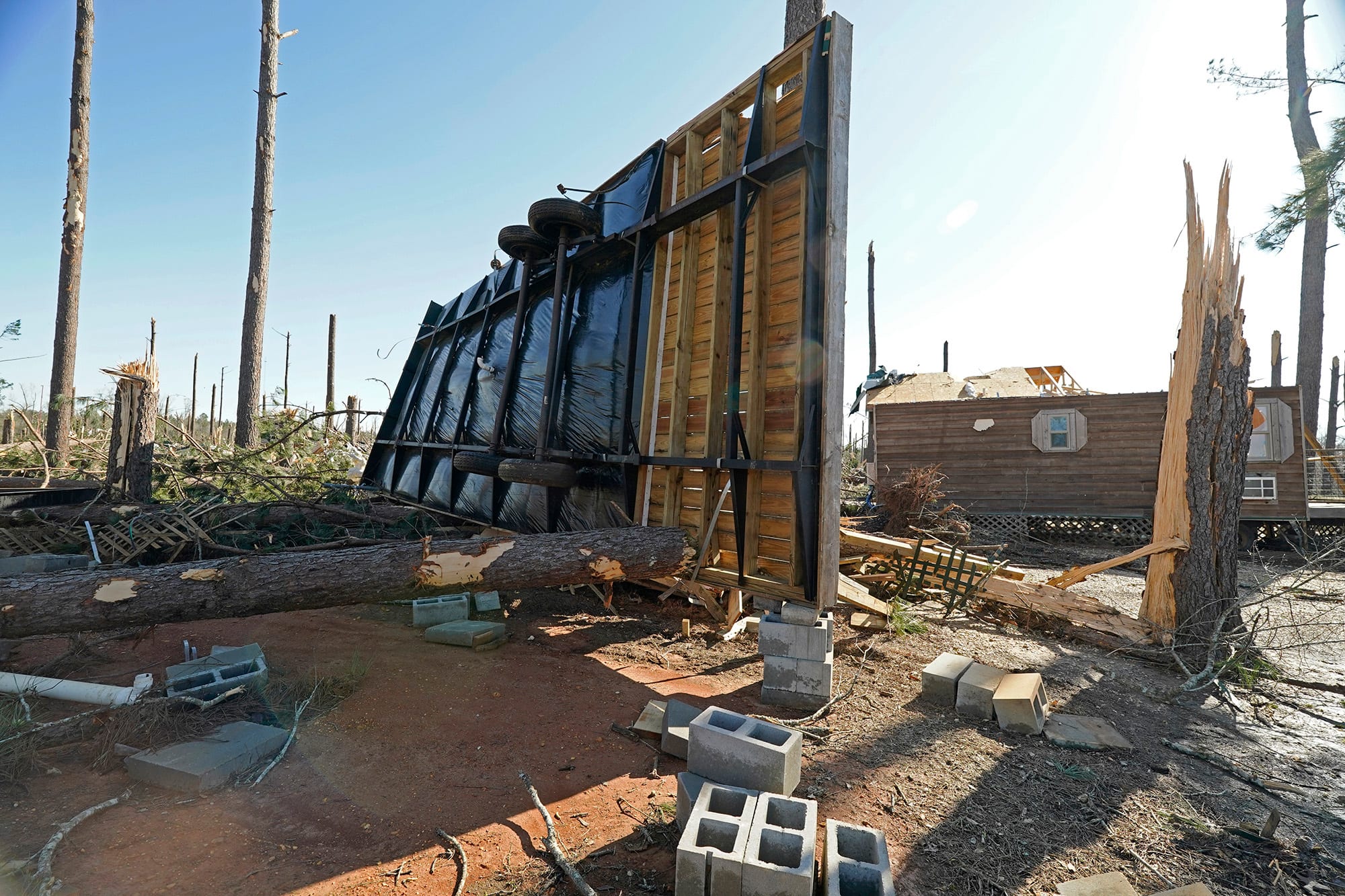 The underside mobile home is seen flipped onto it's side and damaged outside among debris and a fallen tree