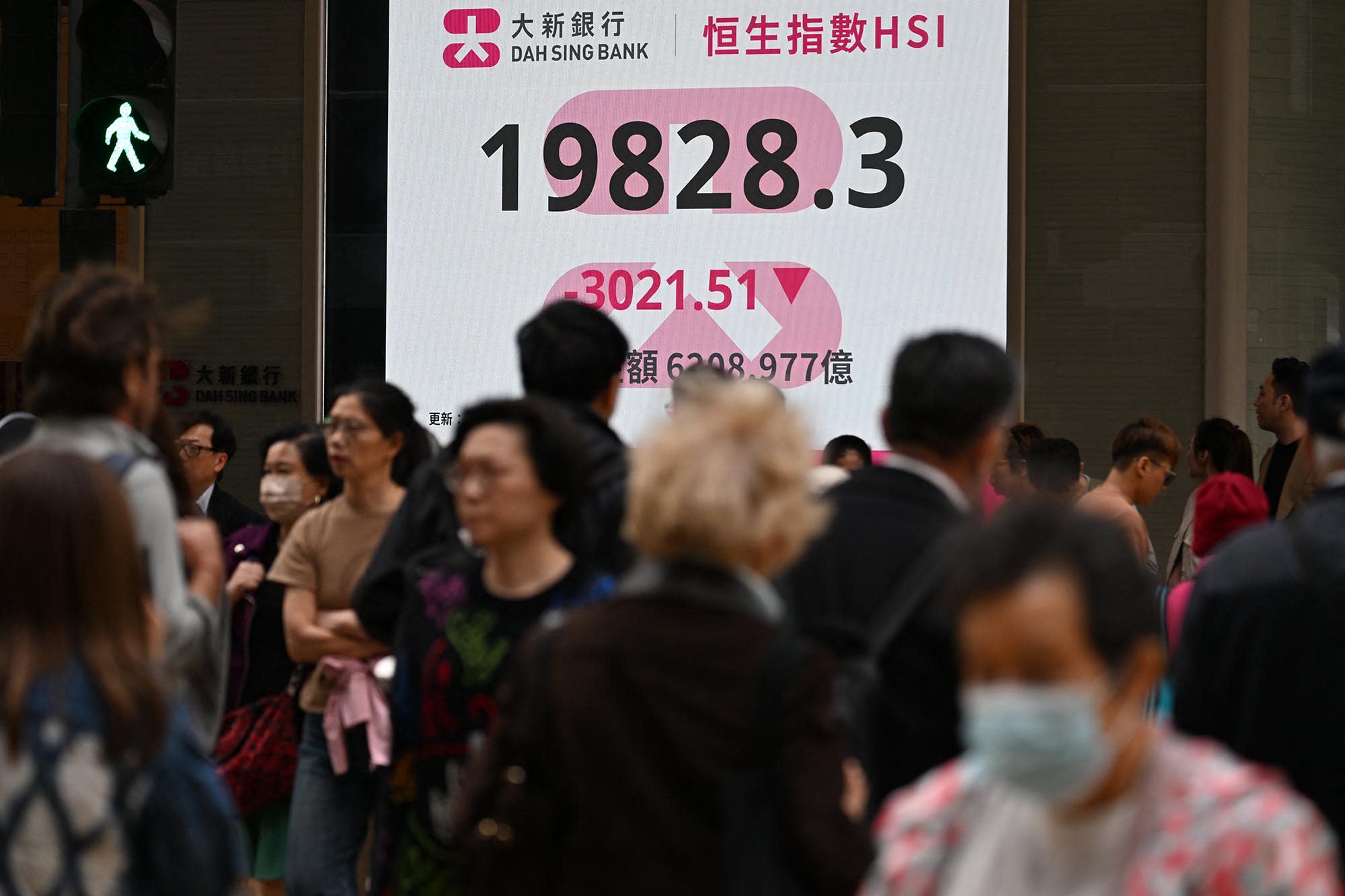 Pedestrians walk past an electronic sign board showing the closing price of the Heng Seng Index in Hong Kong on April 7, 2025. 