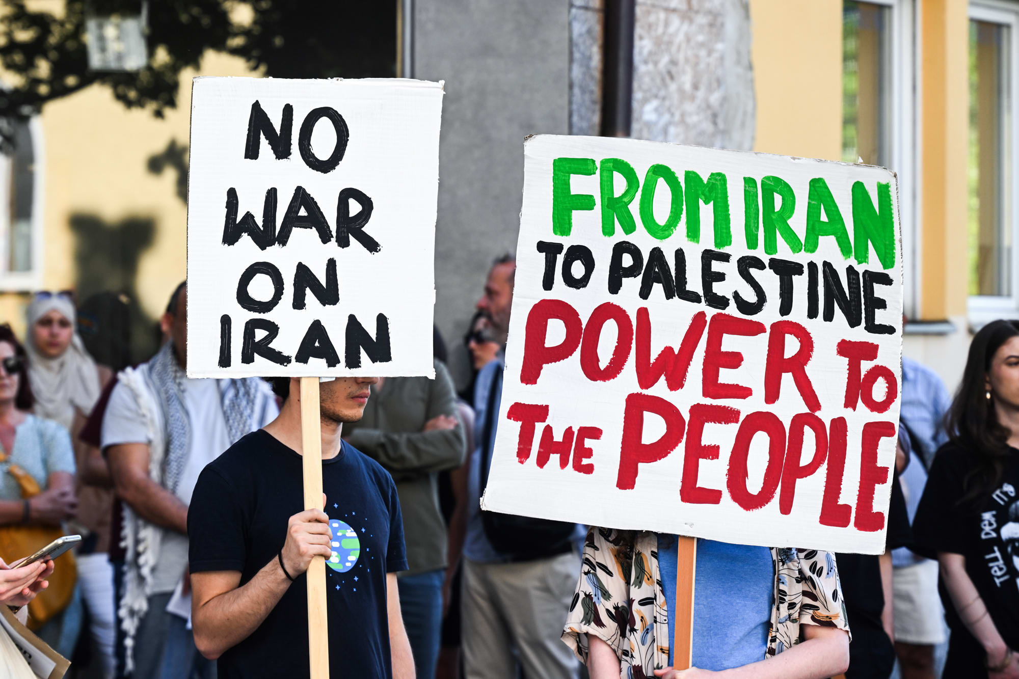 Demonstrators hold signs reading "No War on Iran" and "From Iran to Palestine Power to the People"