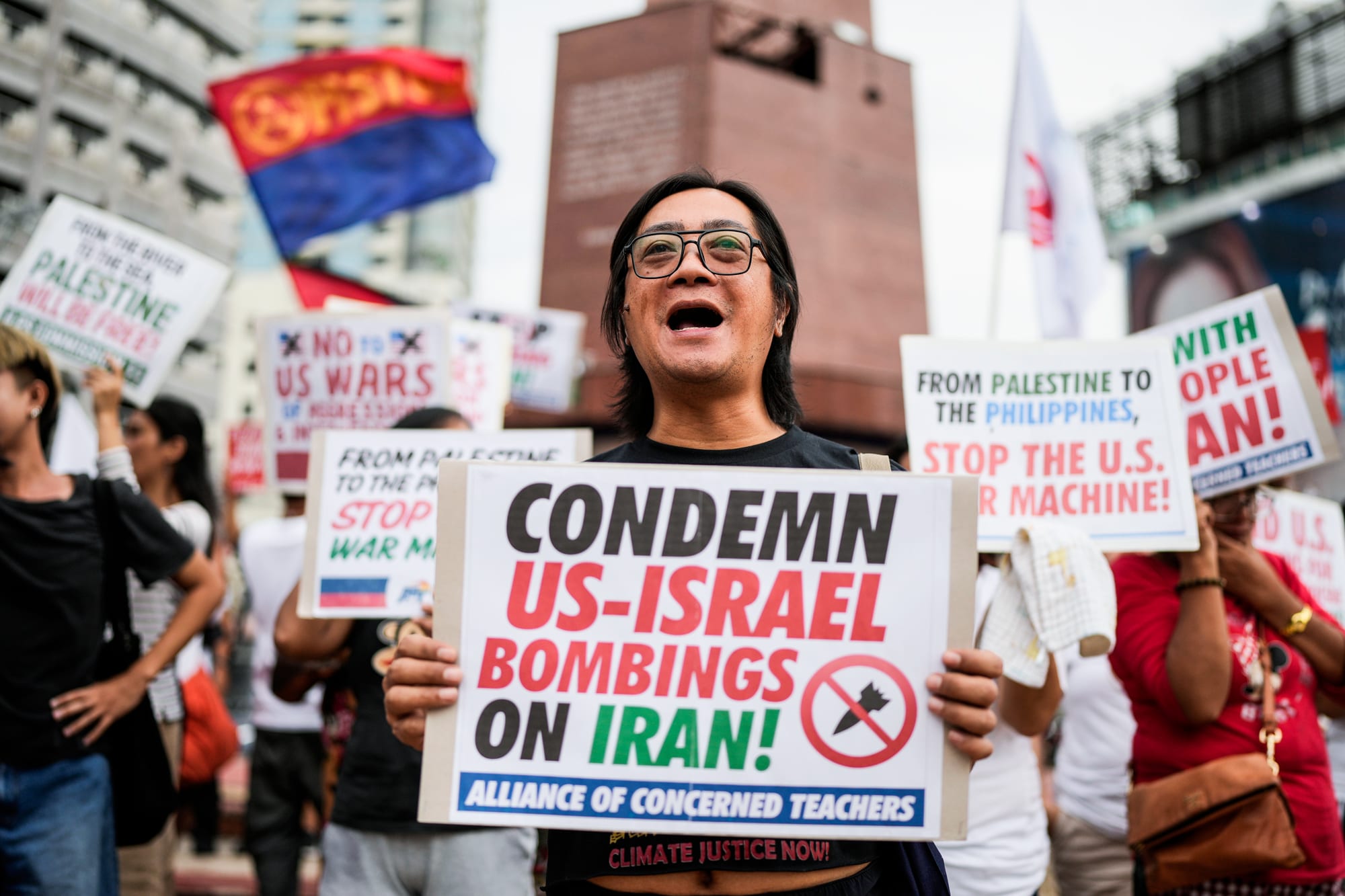 A person holds a sign that says "Condemn US-Israel bombings on Iran"