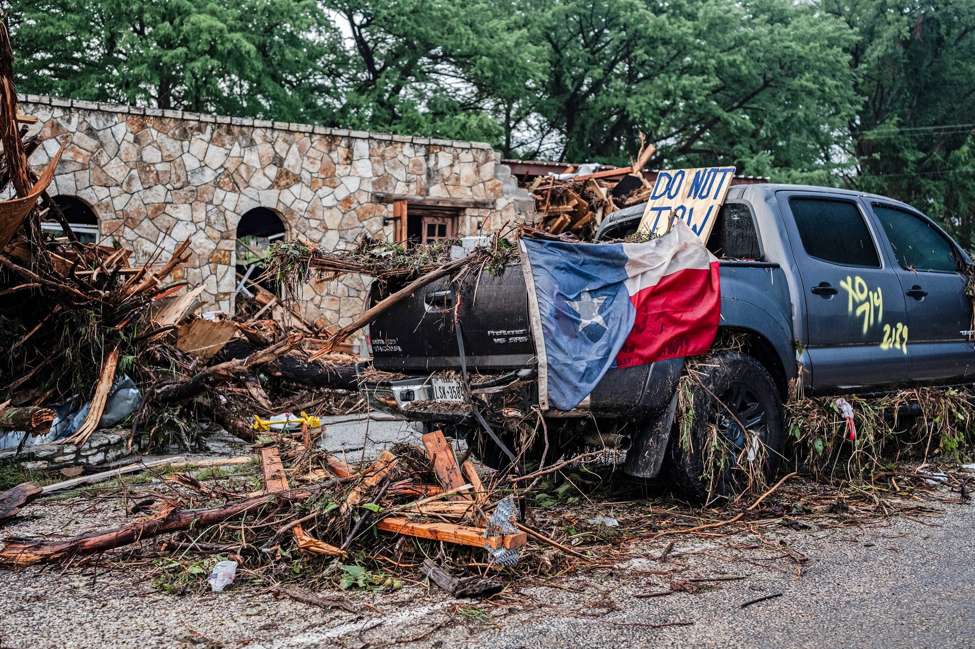 A destroyed SUV draped in a Texas State flag sits next to the road after flash flooding