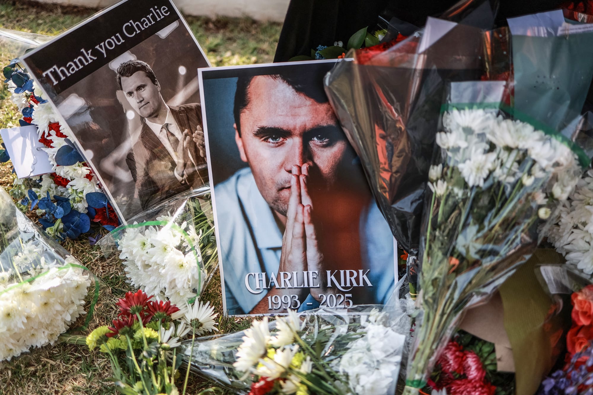 Pictures of Charlie Kirk next to bouquets of flowers on the grass