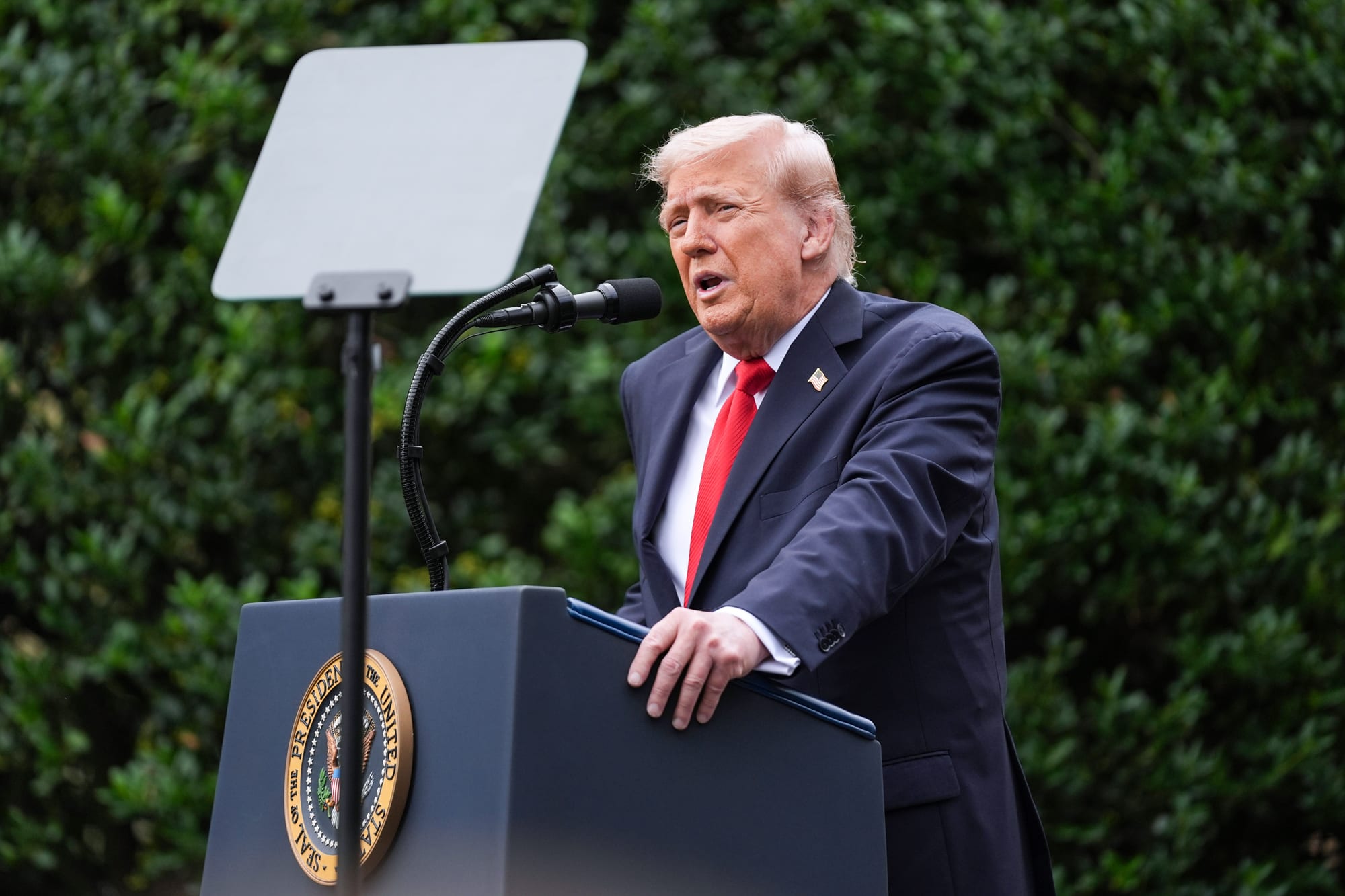 Donald Trump speaks at a podium with a bullet proof glass pane in front of him