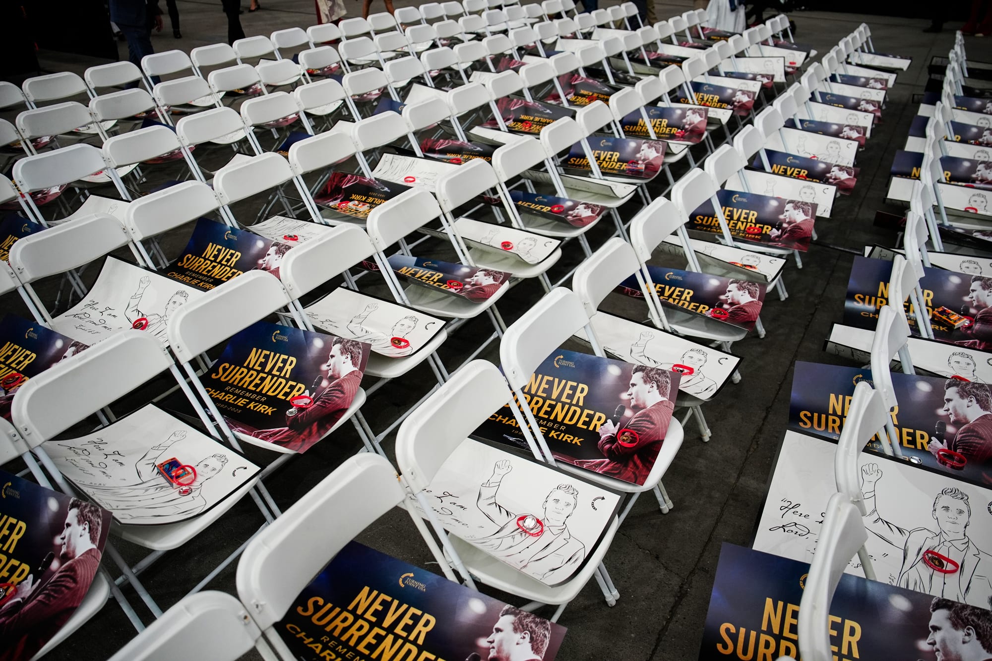 White chairs with Charlie Kirk photos laid on the seats with text that reqads "Never Surrender"