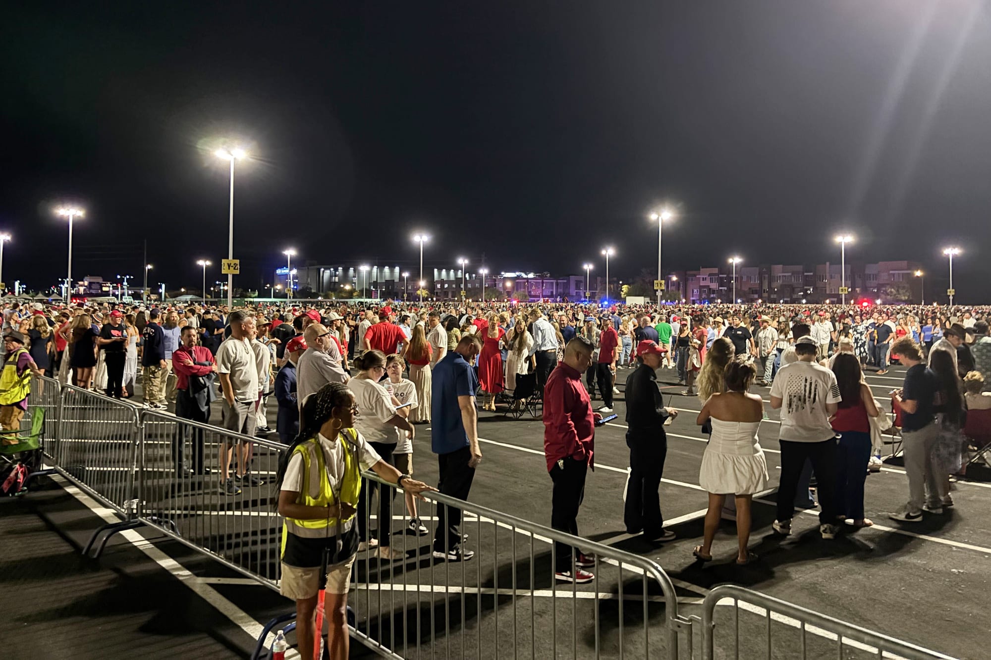 A crowd of people wait outside in a parking lot