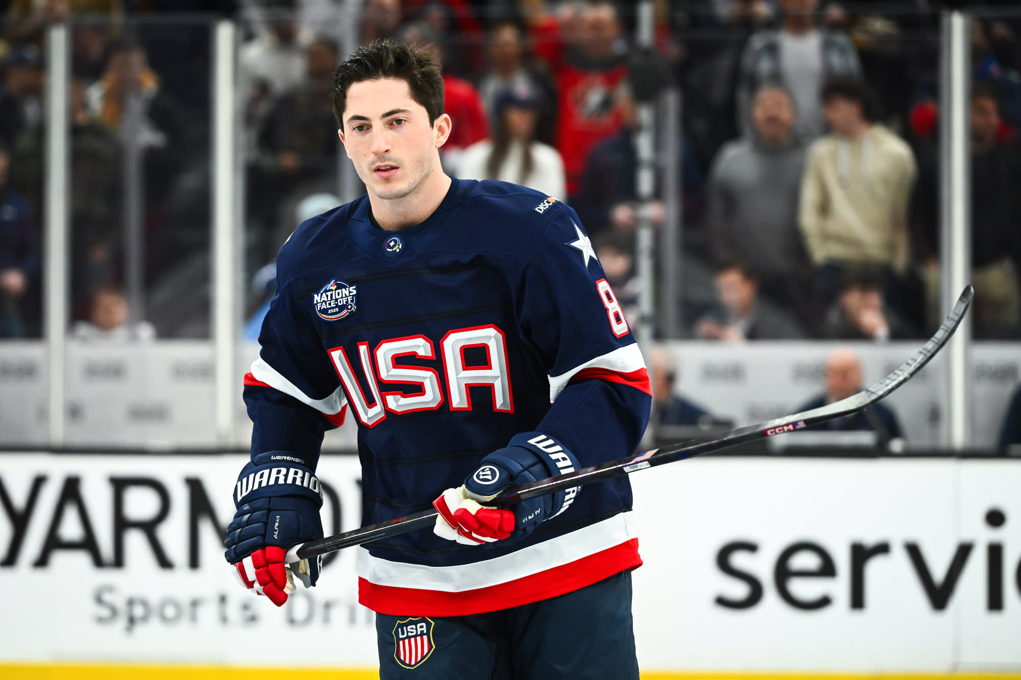 Zach Werenski in the hockey rink in his Team USA uniform holding a hockey puck