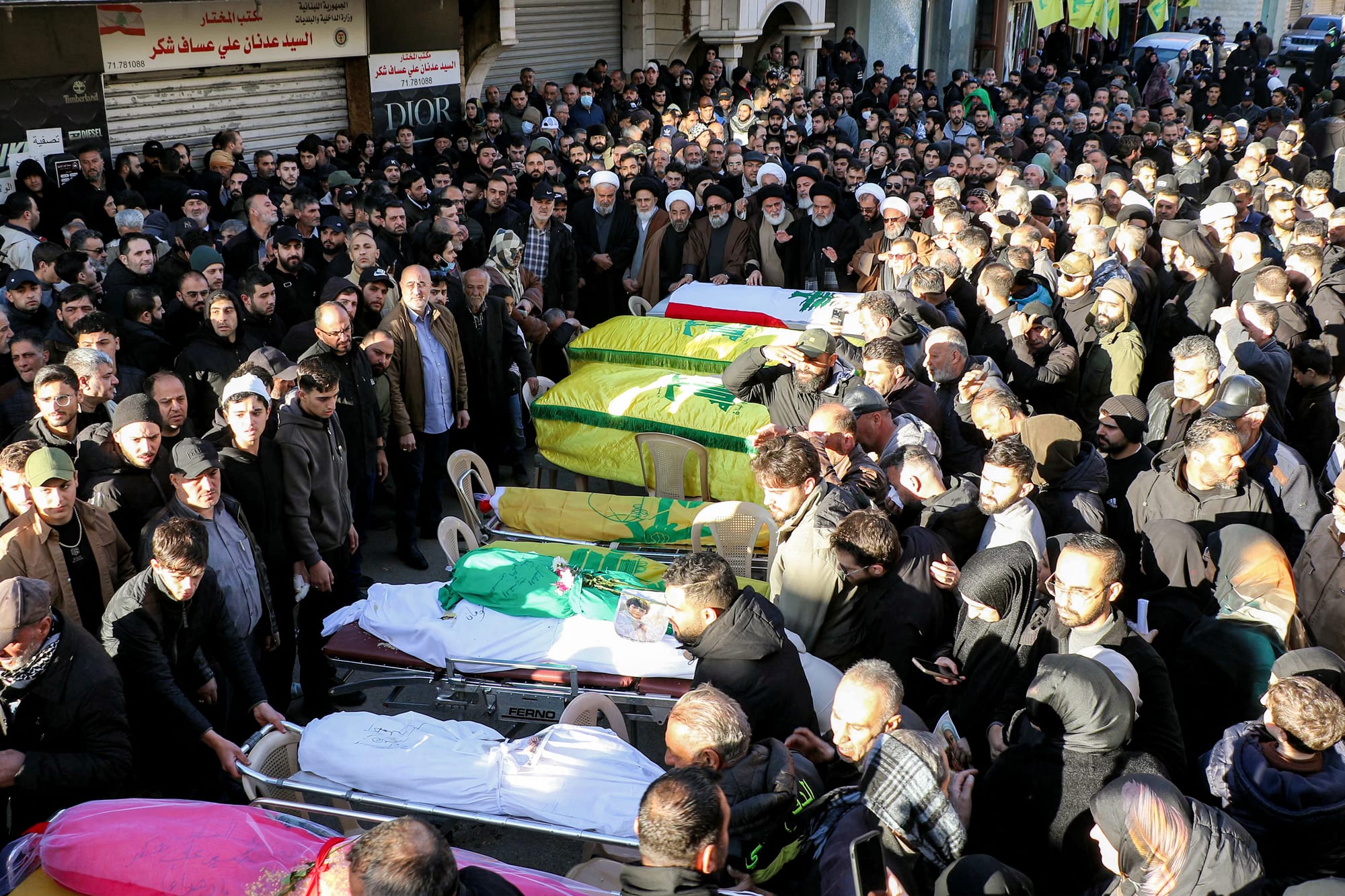 Bodies covered in tarp and caskets are carried through a large crowd of people