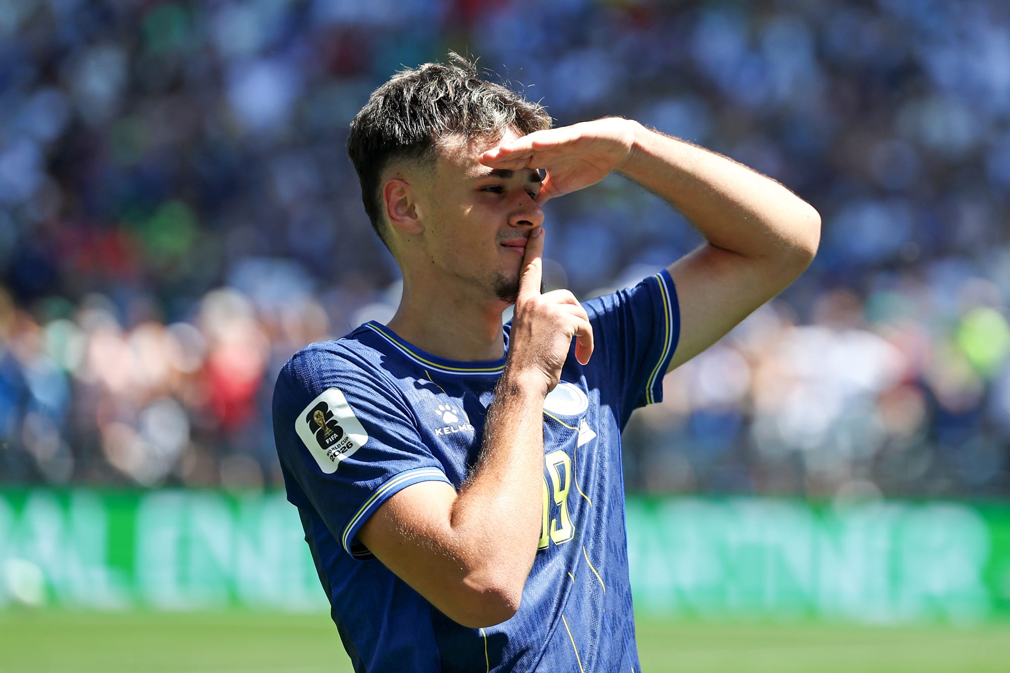 Kerim Alajbegovic uses one hand as a visor on his forehead, and using his other hand puts a finger on his lips in a "shh" gesture