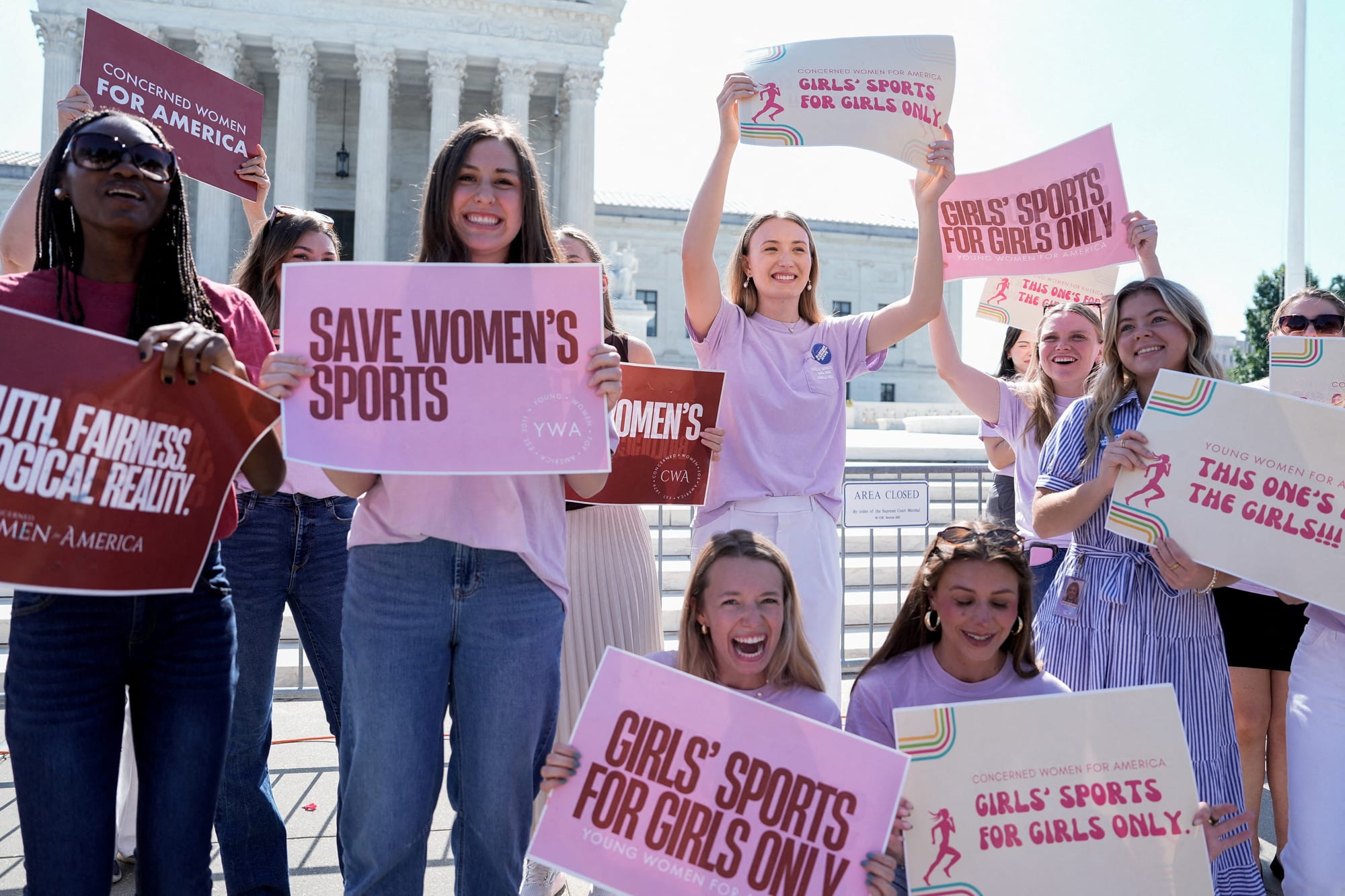 People hold signs in front of the Supreme Court that say "save women's sports", "girls's sports for girls only", etc