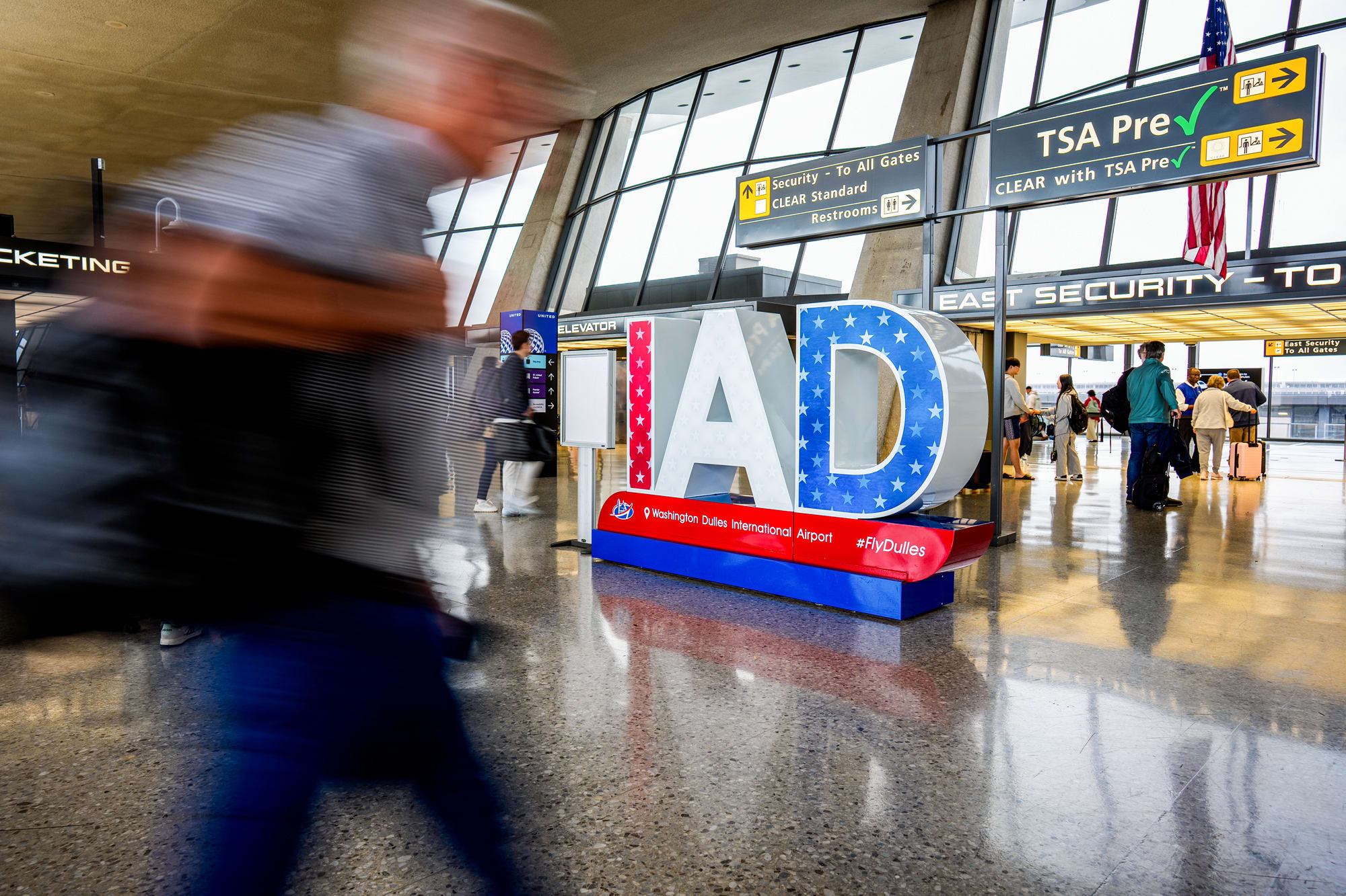 A blurred individual walks past large "IAD" lettering depicting the airport code for Washington Dulles International Airport is displayed in the airport's main concourse