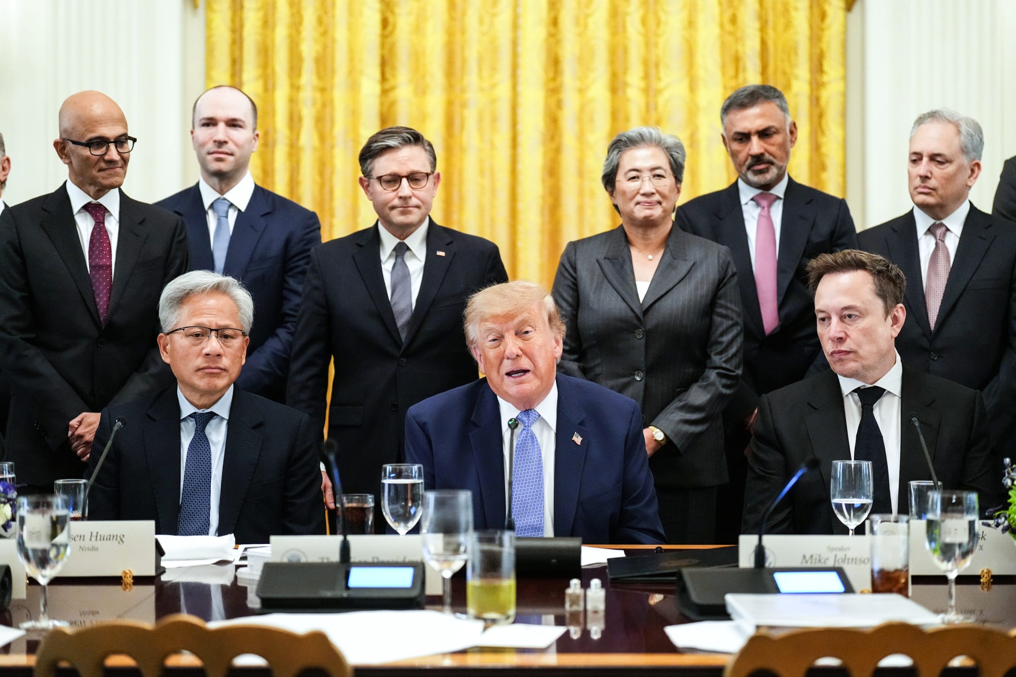 Donald Trump sits at a table next to Jensen Huang, left, and Elon Musk, while Mike Johnson and others stand behind them.