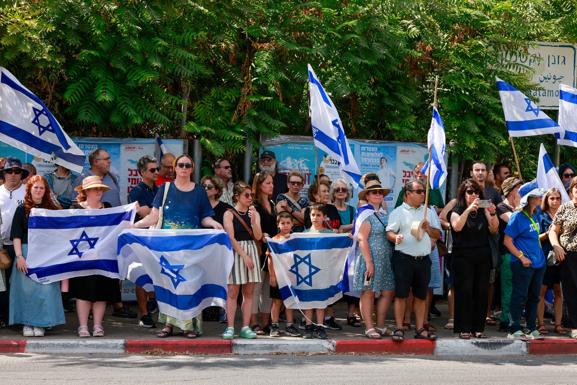 People line a sidwalk holding Israeli flags