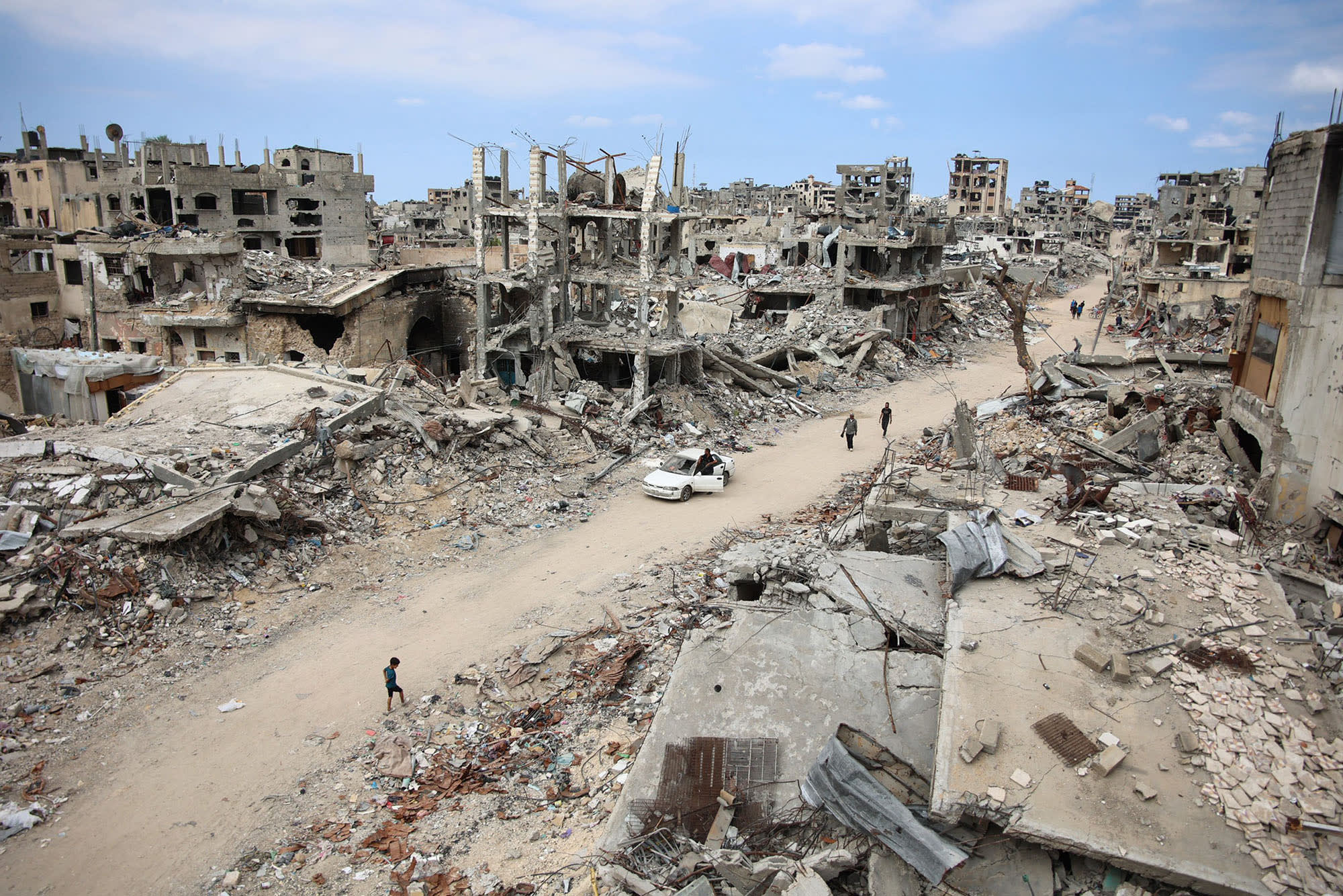 Displaced Palestinians walk on a dirt road lined with rubble in the Shujaiya neighborhood of Gaza City on Oct. 7, 2024.