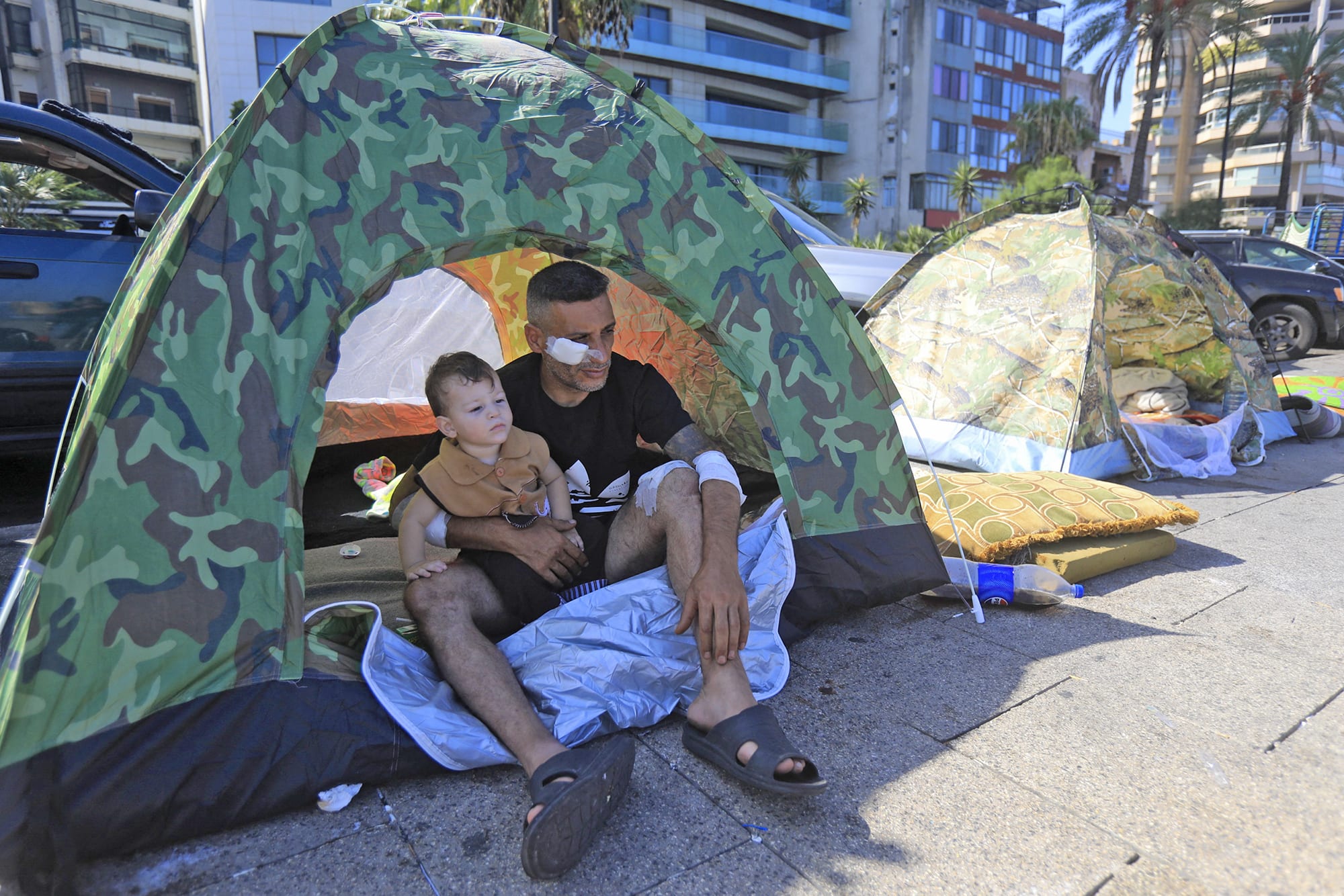 A wounded displaced man sits with his child inside their tent in central Beirut's seaside promenade on Oct. 7, 2024.