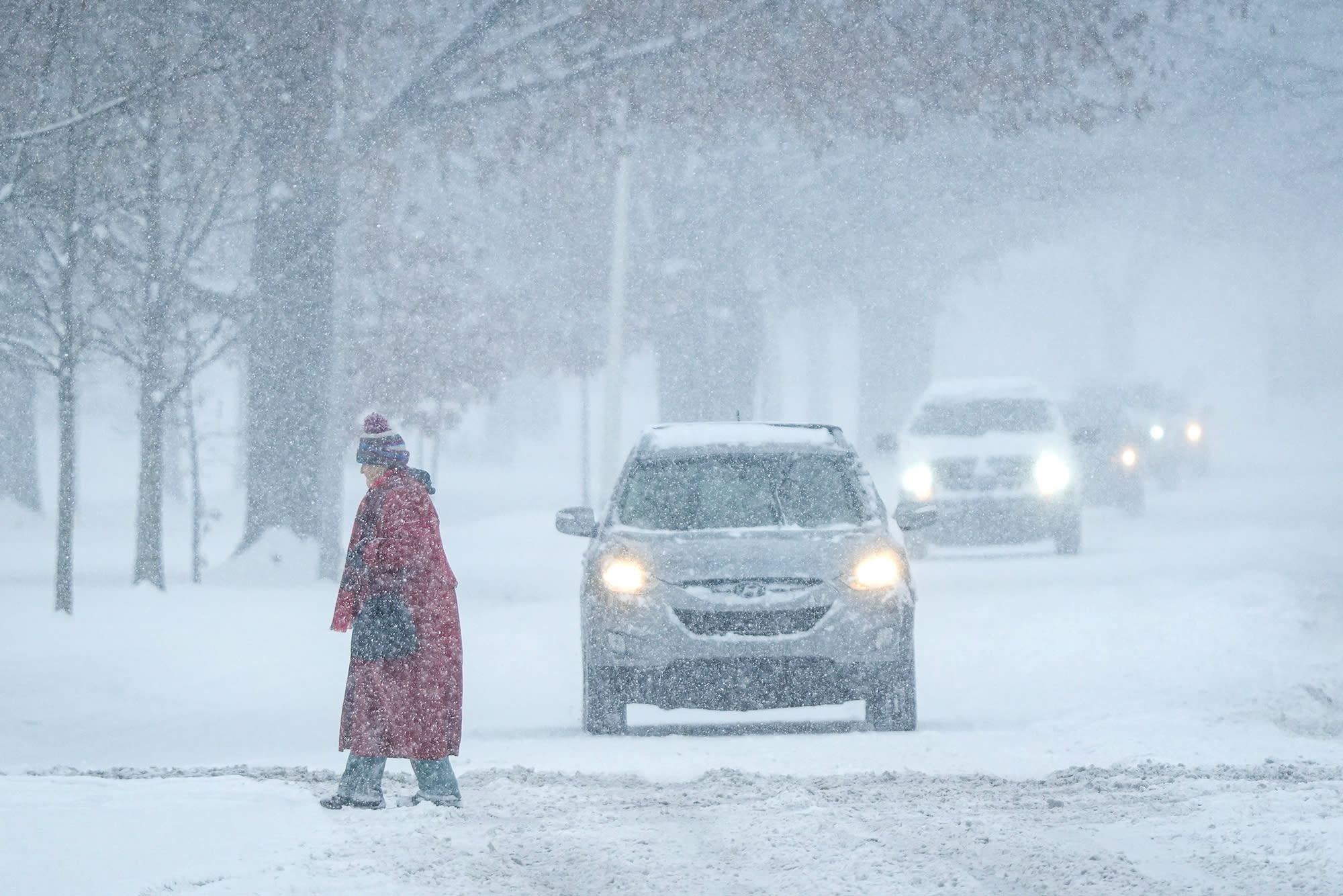 A pedestrian crosses the street as cars wait during a blizzard