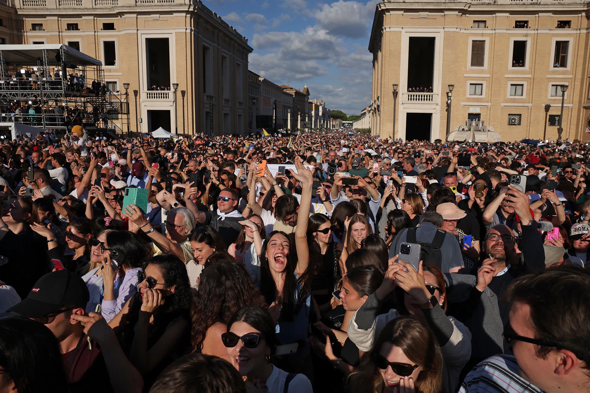Crowds gathered around St Peter's Square react as white smoke rises from the chimney on the roof of the Sistine Chapel