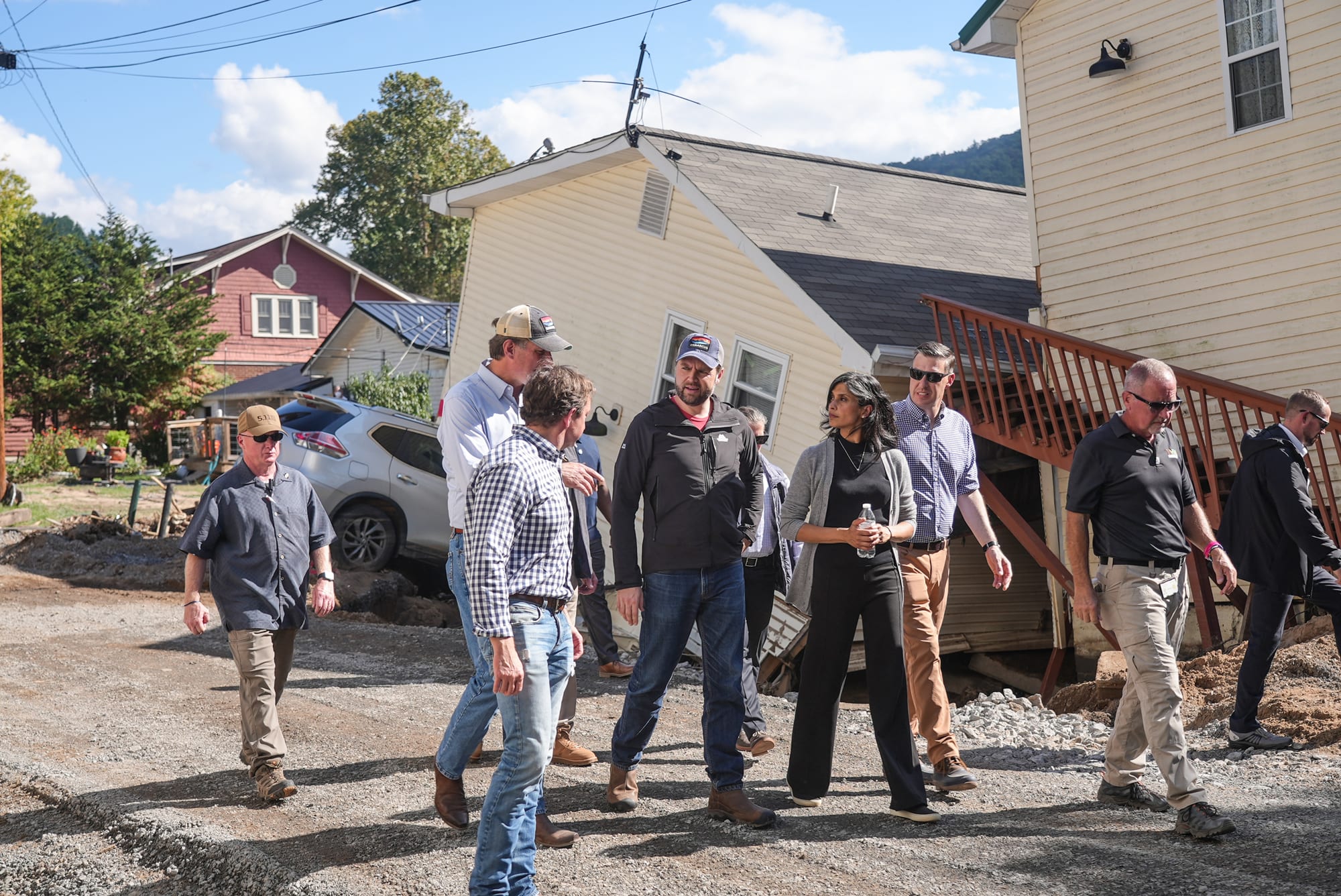 JD Vance, center, and others walk past damage from storm Helene on the street