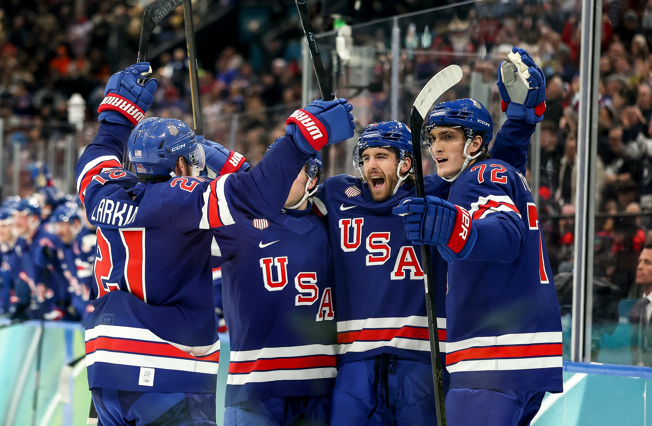 Four Team USA hockey players in red, white, and blue uniforms celebrate on the ice.