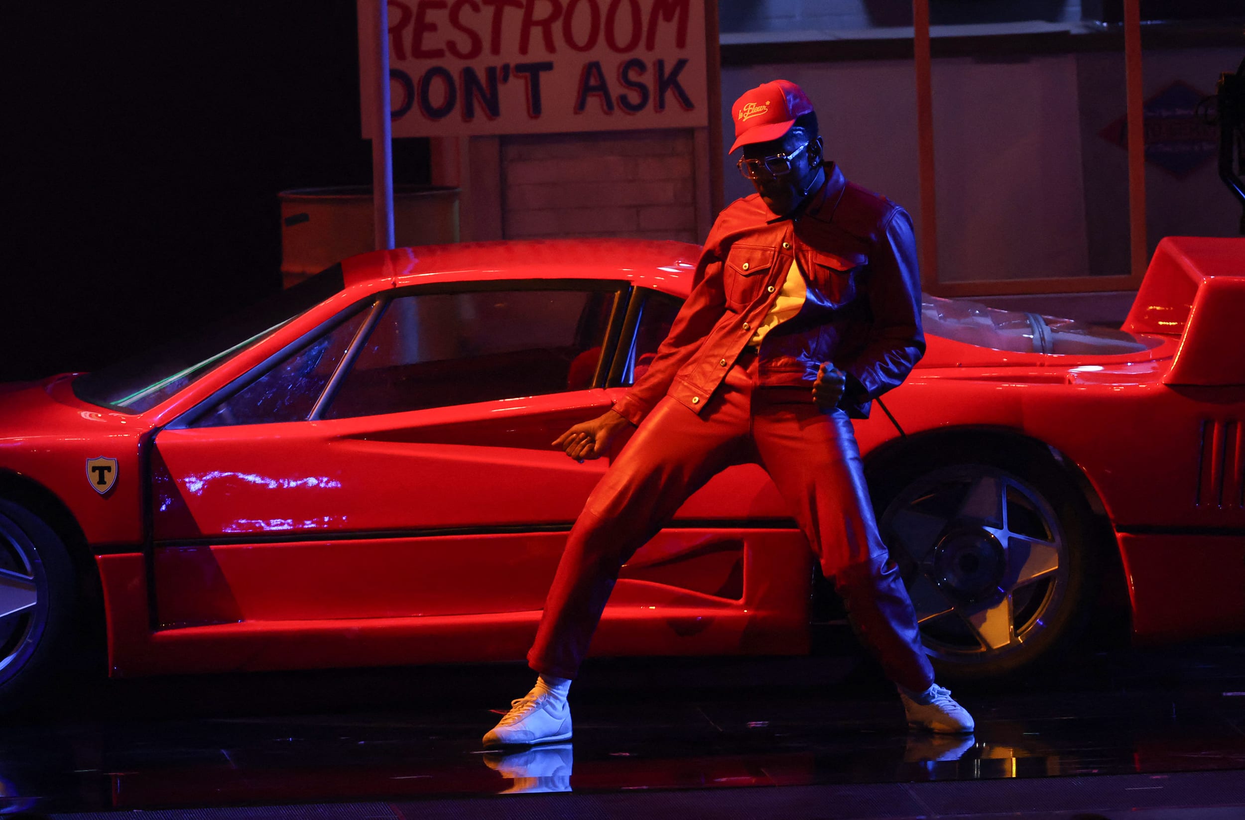 Tyler the Creator performing onstage in front of a red sports car.