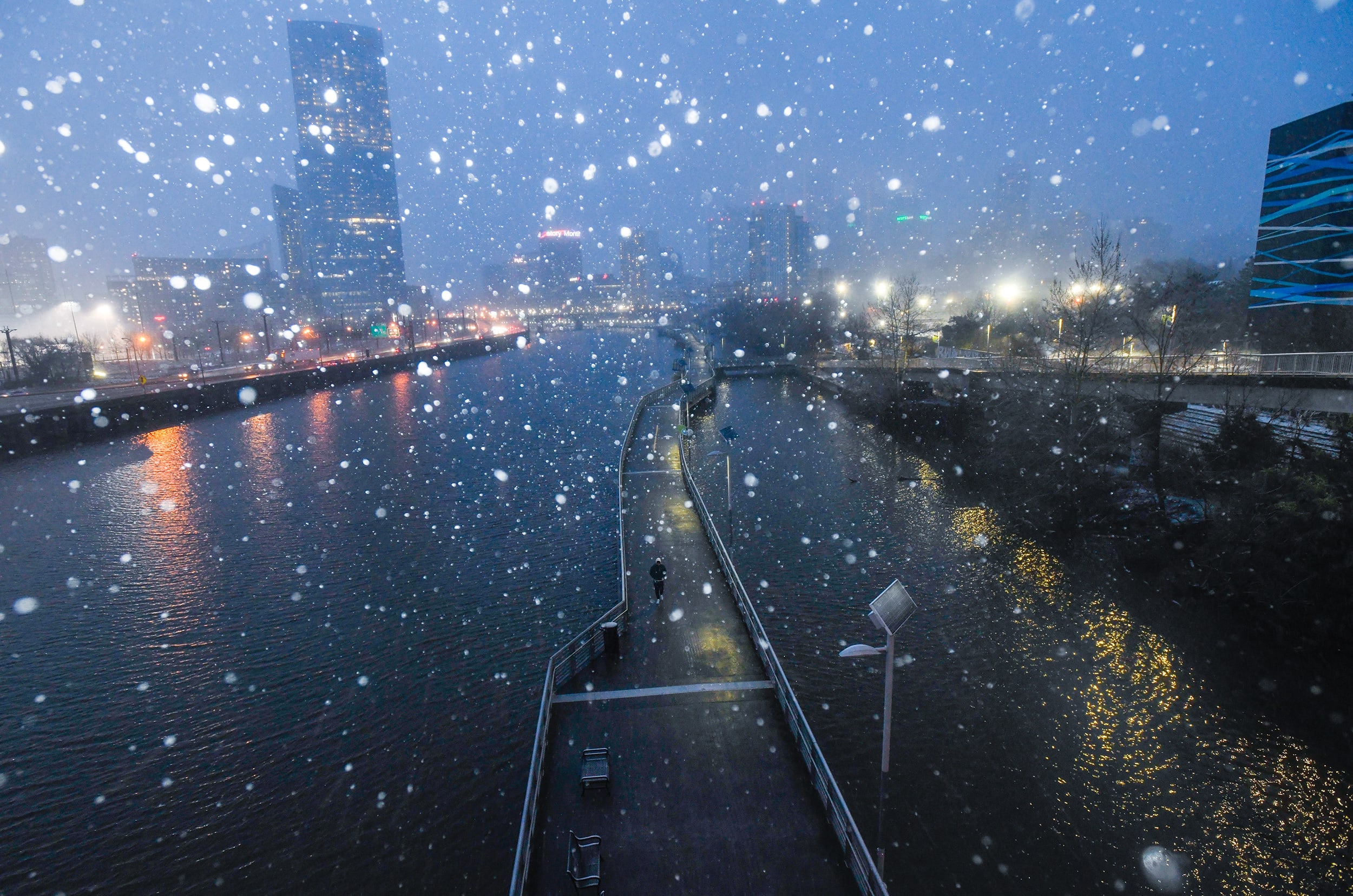A footbridge over water in the water at dusk is visible through snowflakes that appear in soft focus. 