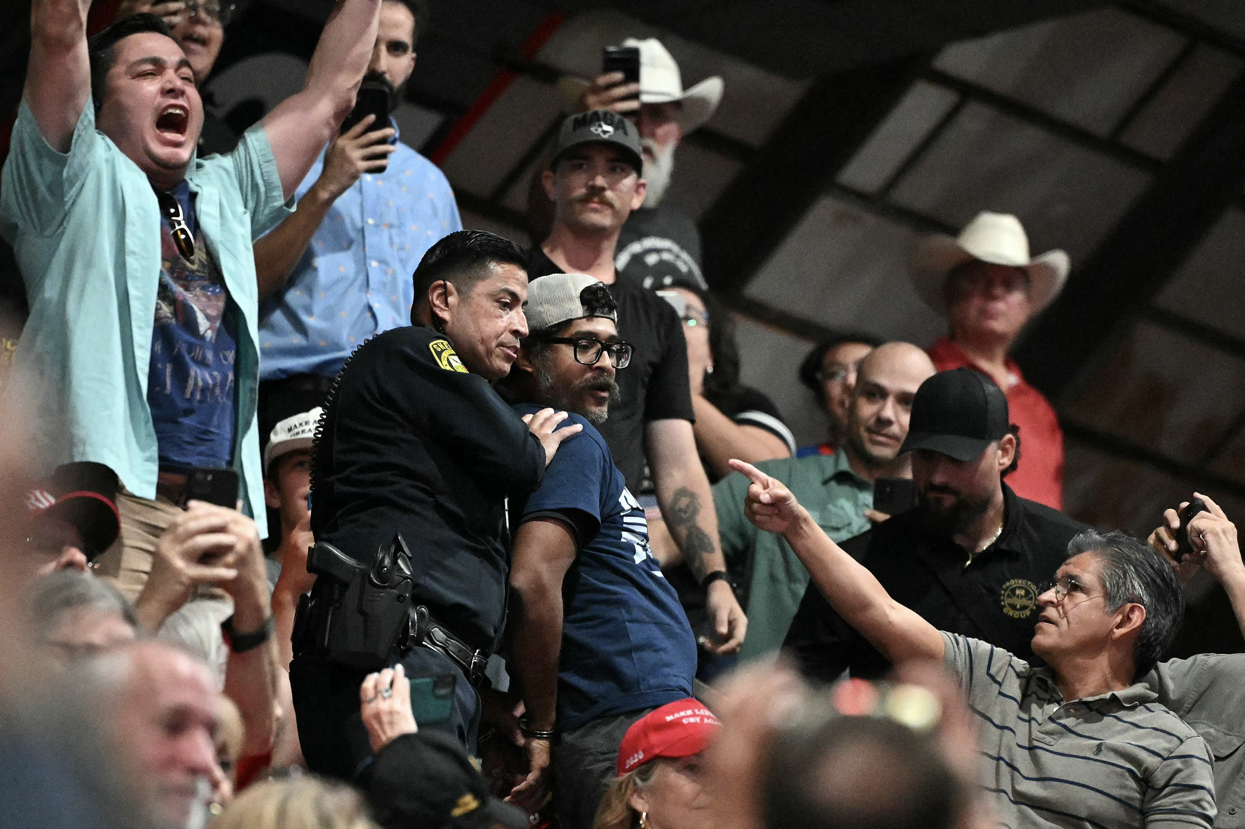 A police officer holds a protestor's arms behind his back during an indoor political rally.