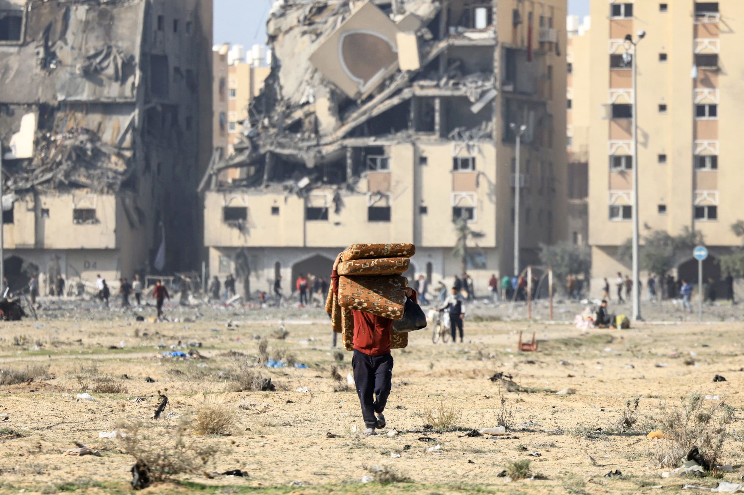 A person walks away from a destroyed residential building while carrying belongings