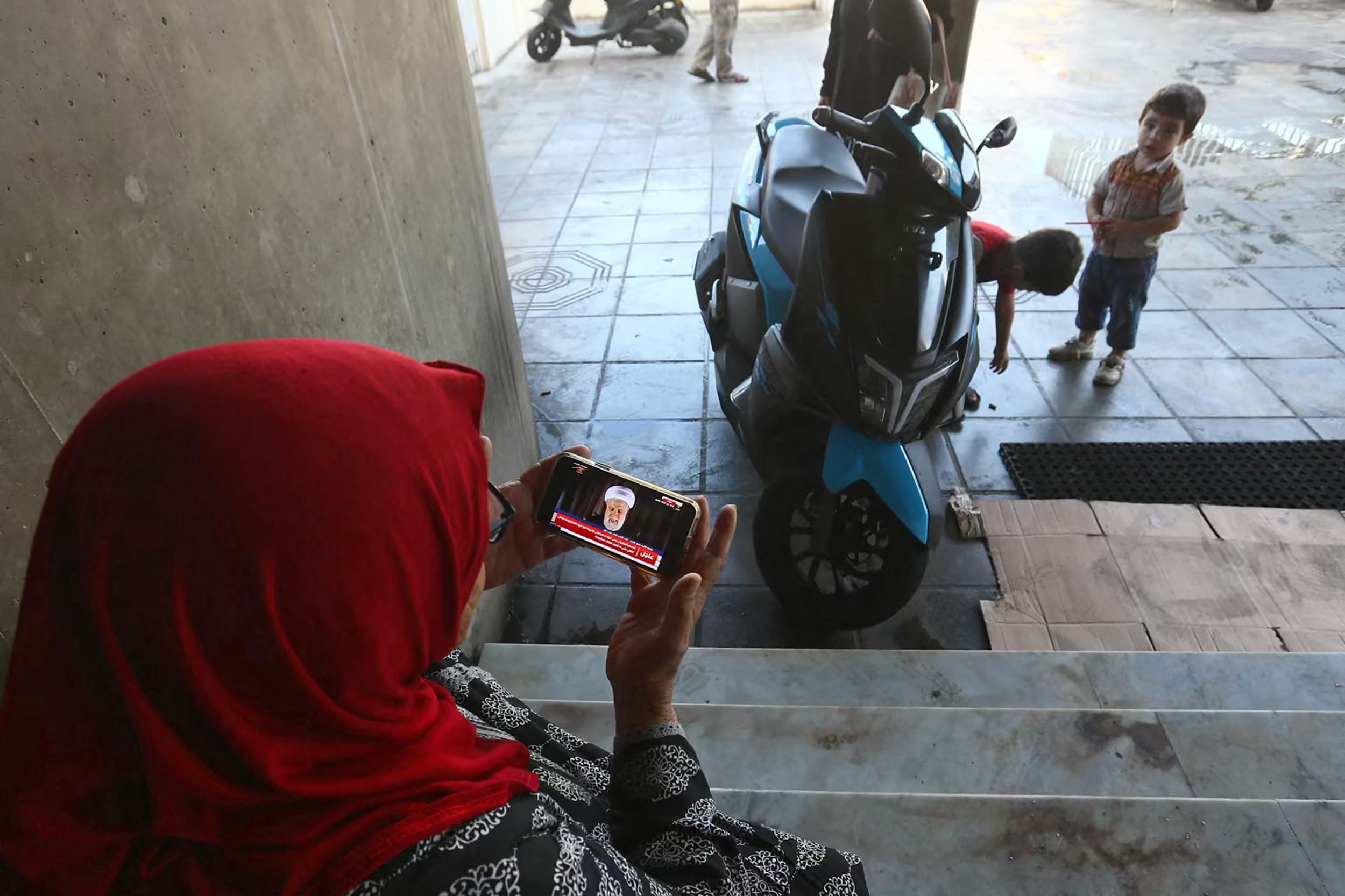 A displaced woman wathces Hezbollah Vice Hezbollah Secretary General Naim Qassem's speech on her phone