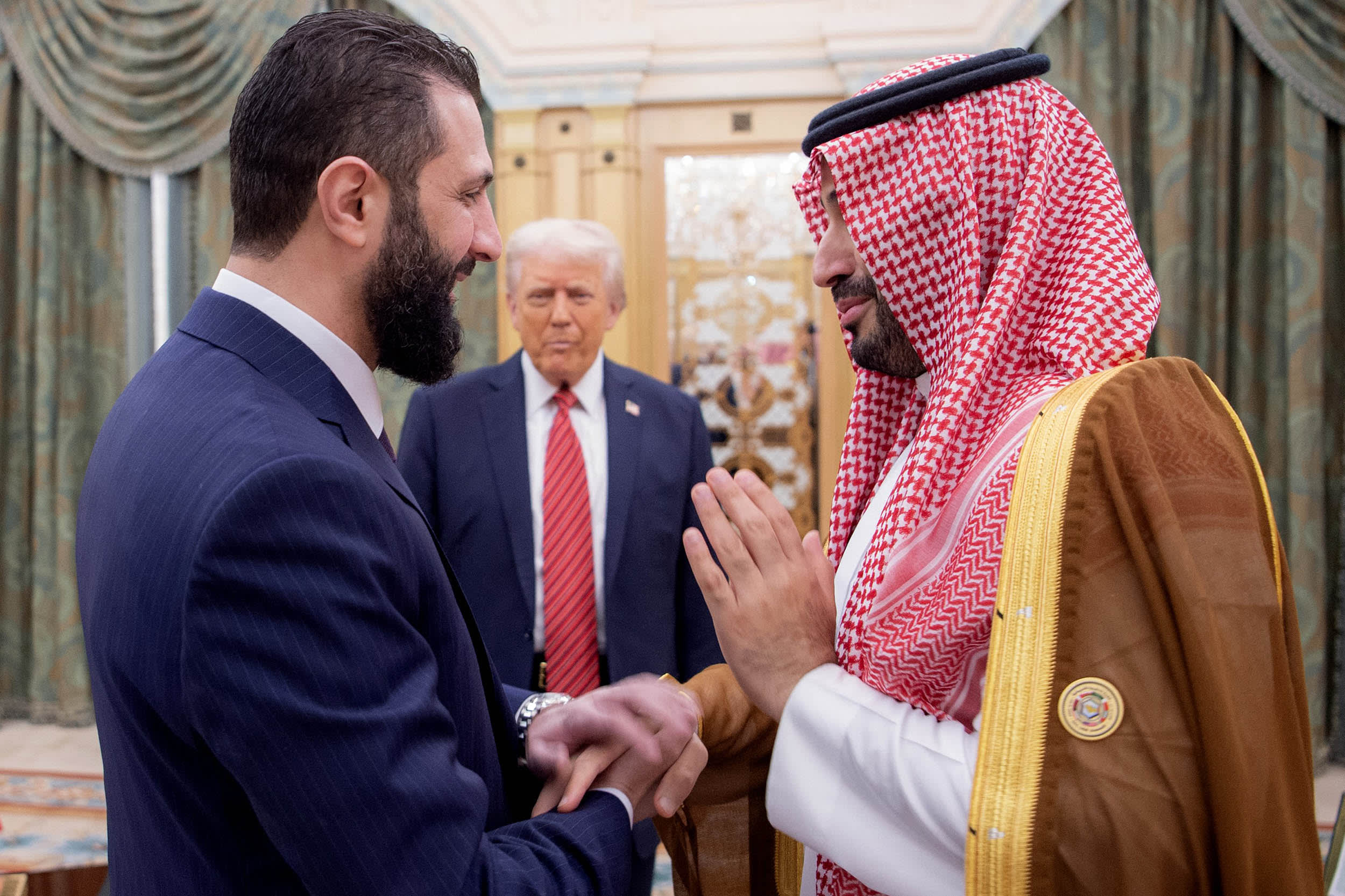 Saudi Crown Prince Mohammed bin Salman shakes hands with Syria's interim president Ahmed al-Sharaa as US President Donald Trump looks on.