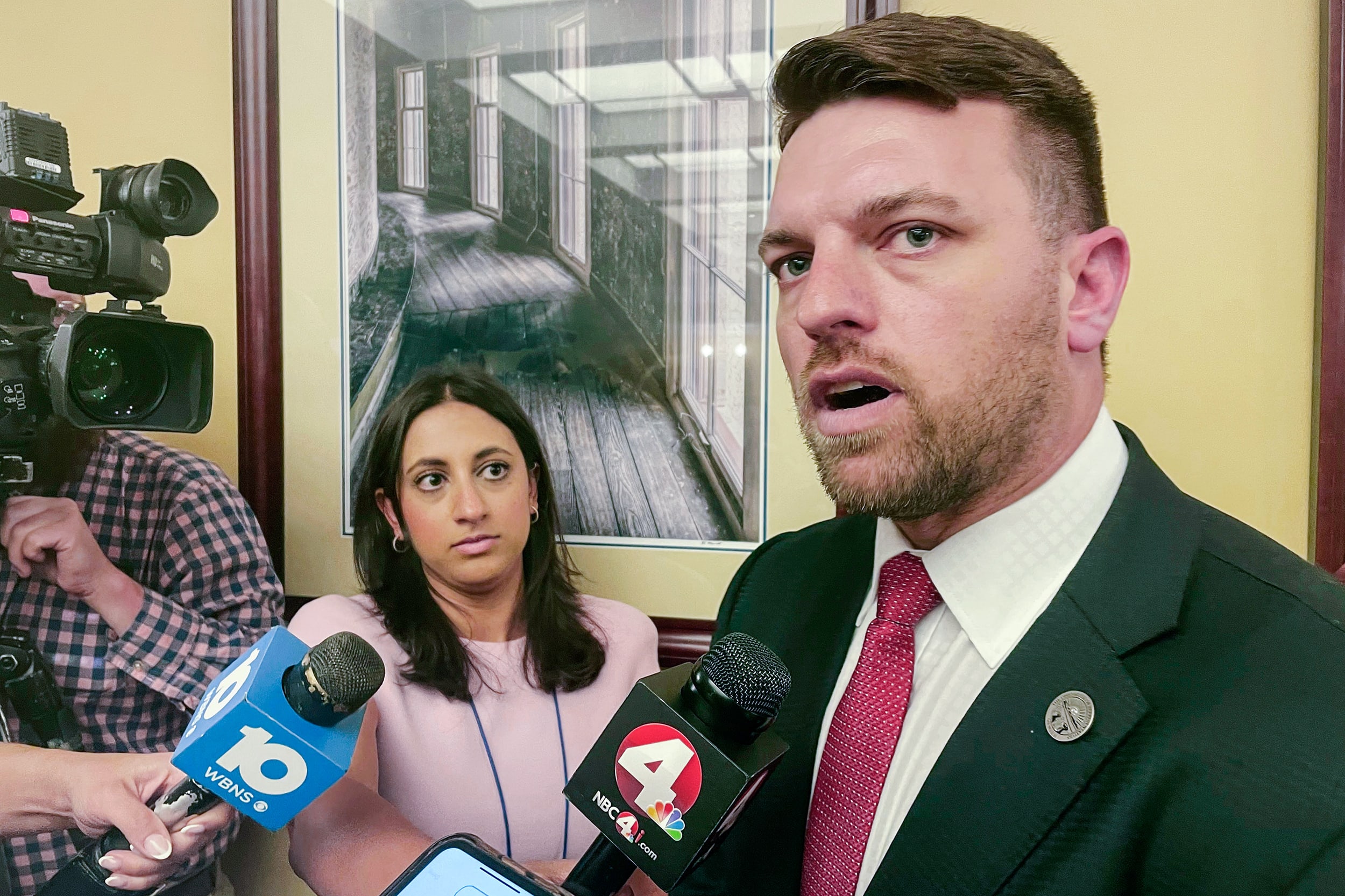 Jay Edwards speaks into a television reporter's microphone as other reporters look on.