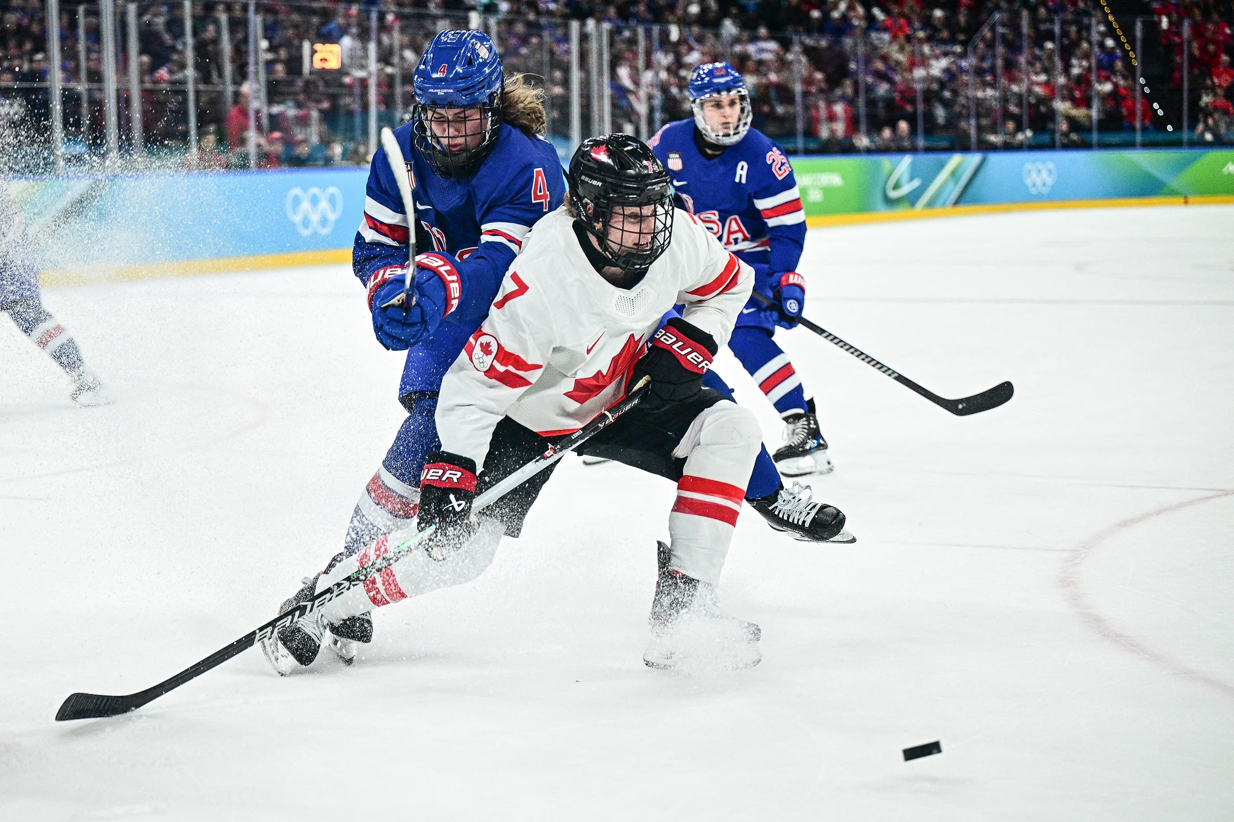 Three women ice hockey players are seen on the ice during gameplay.