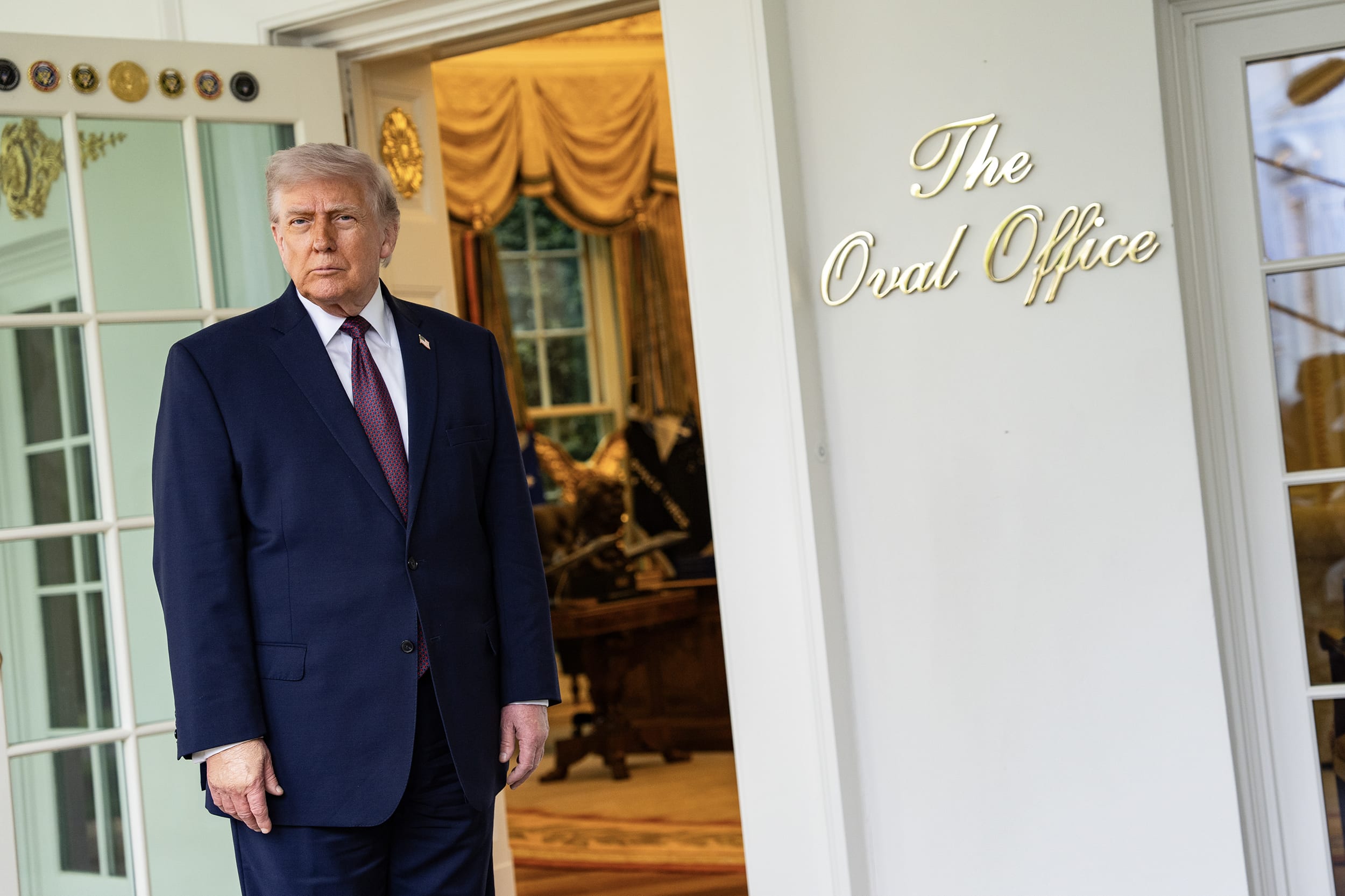 Donald Trump looks directly into the camera while standing in front of the exterior door to the Oval Office.