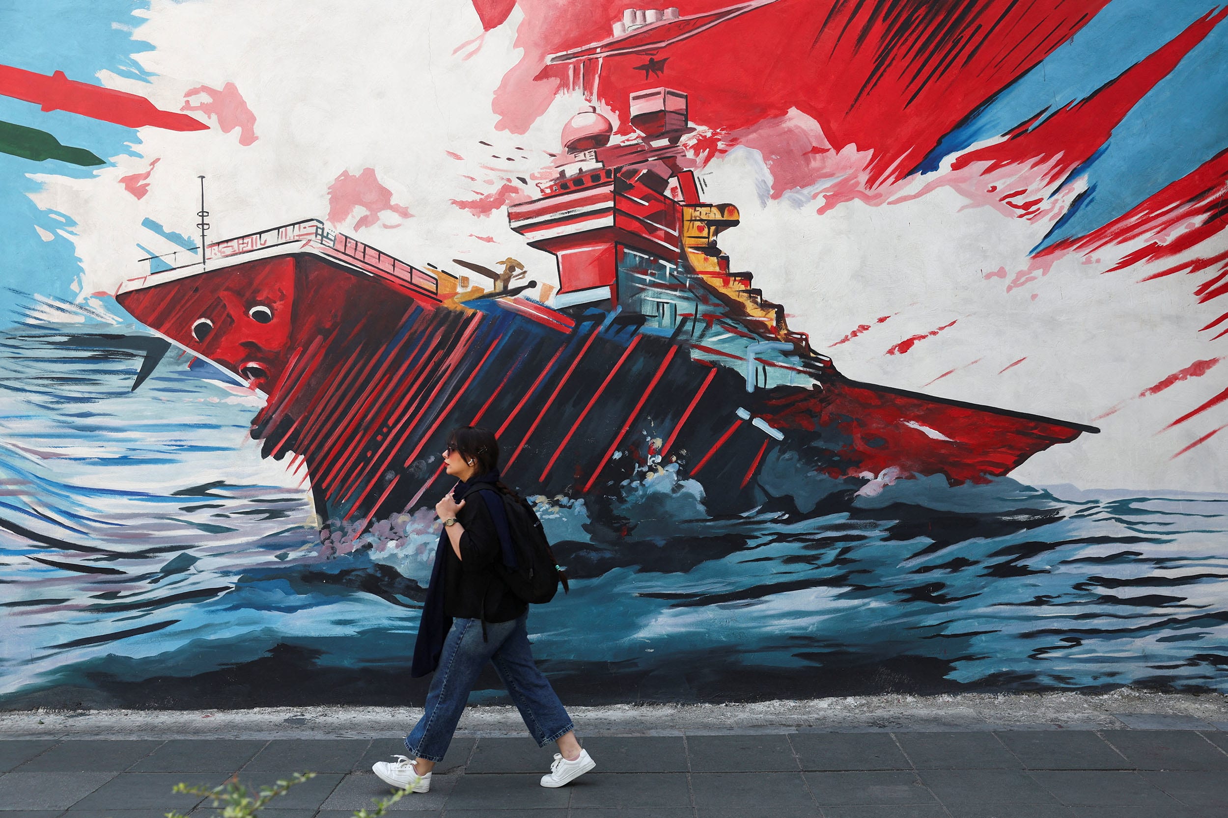 An Iranian woman walks next to an anti-U.S mural on a street in Tehran