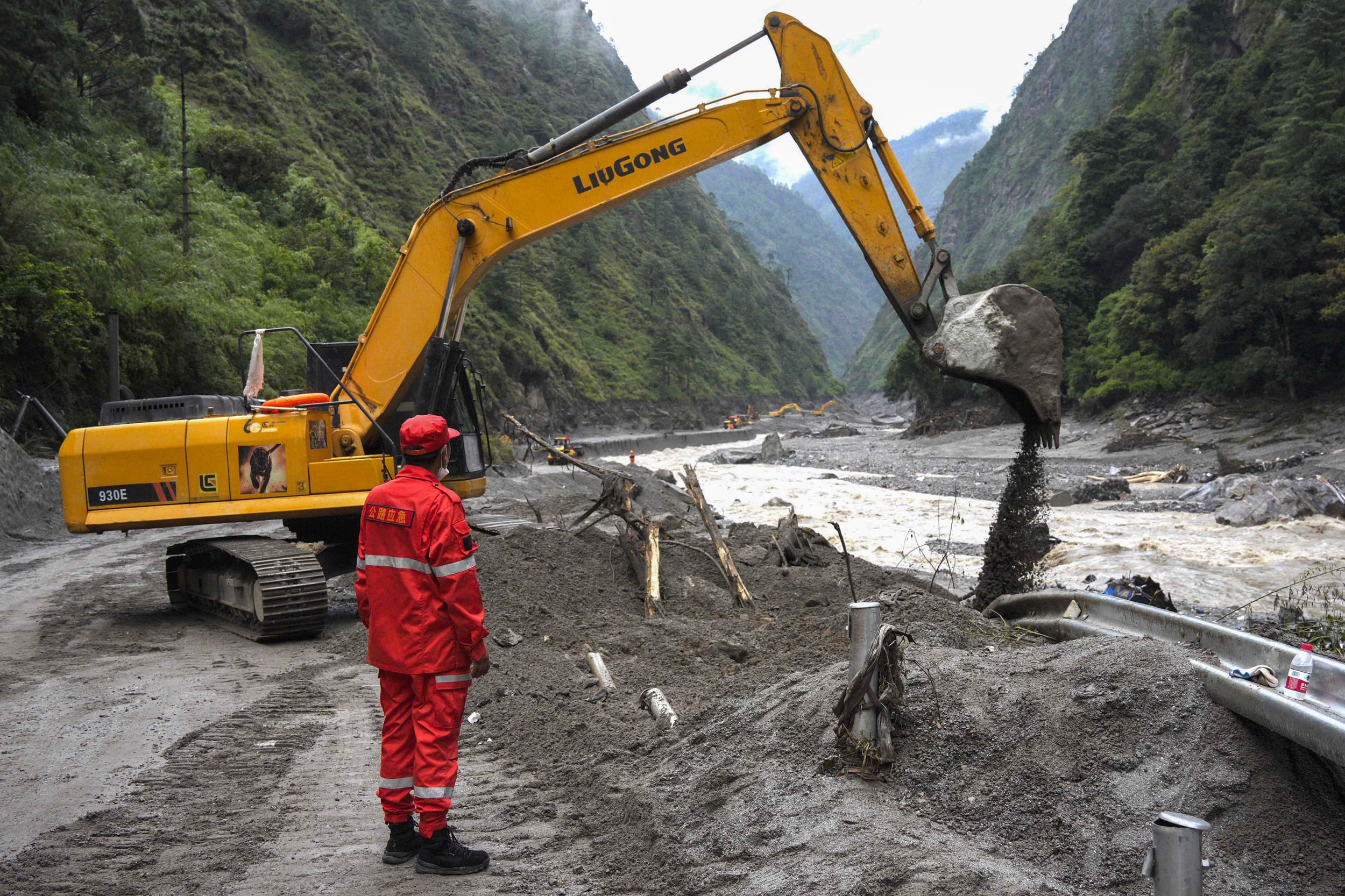 Excavators and loaders clear debris in a muddy street.