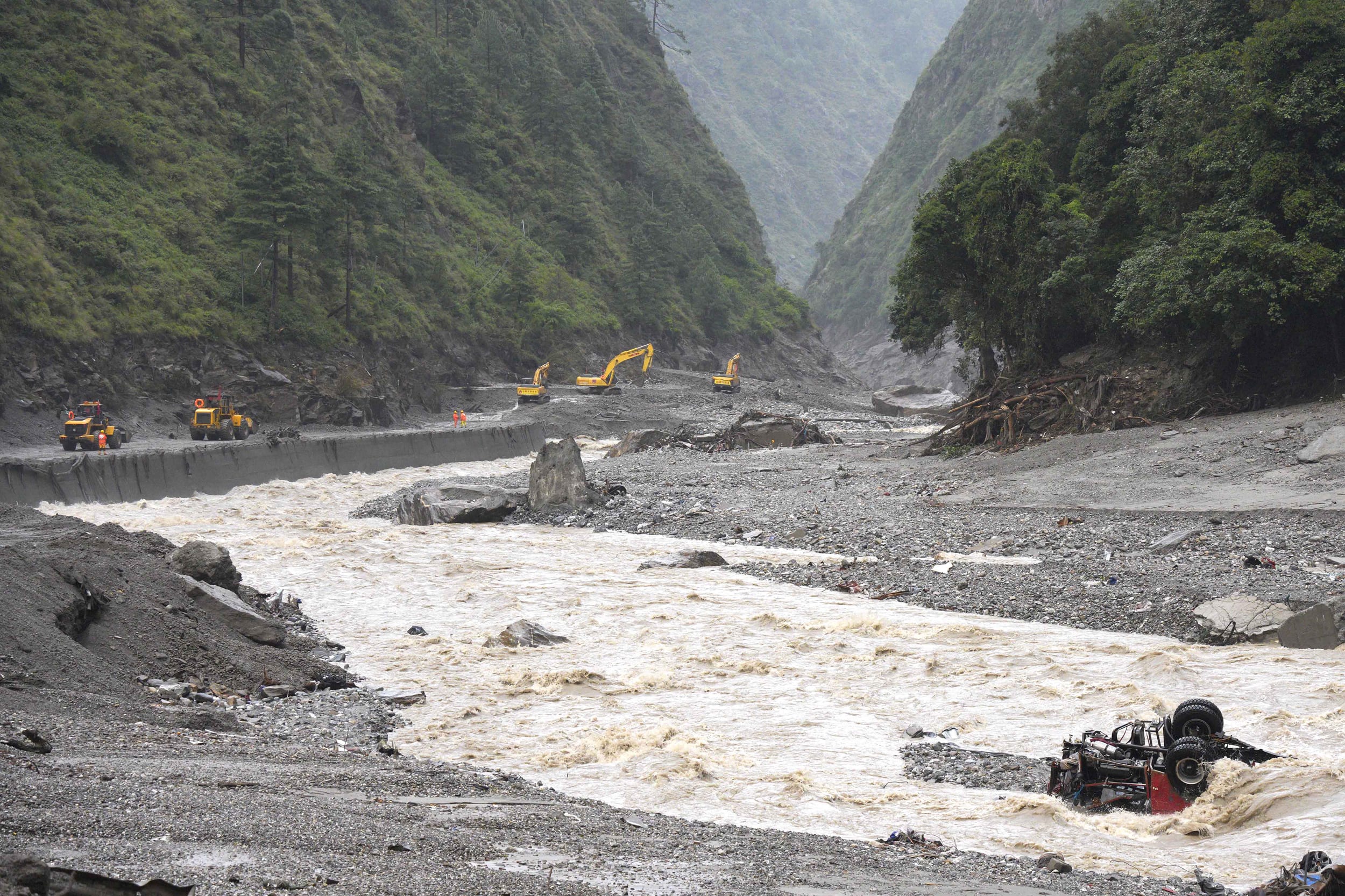 Excavators and loaders clear debris on a damaged road.