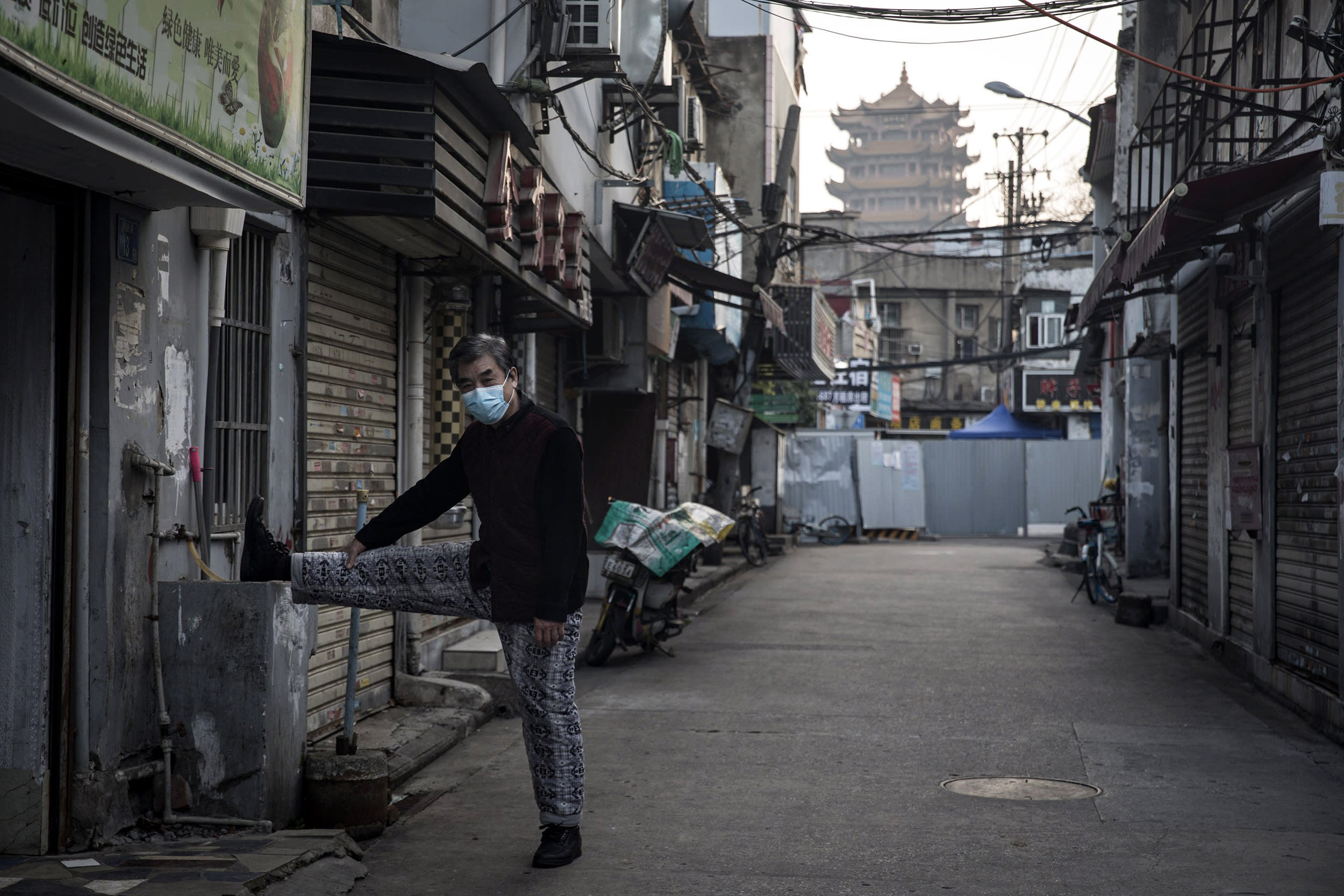 Image: A man stretches while exercising near a makeshift barricade wall in Wuhan on March 4, 2020.