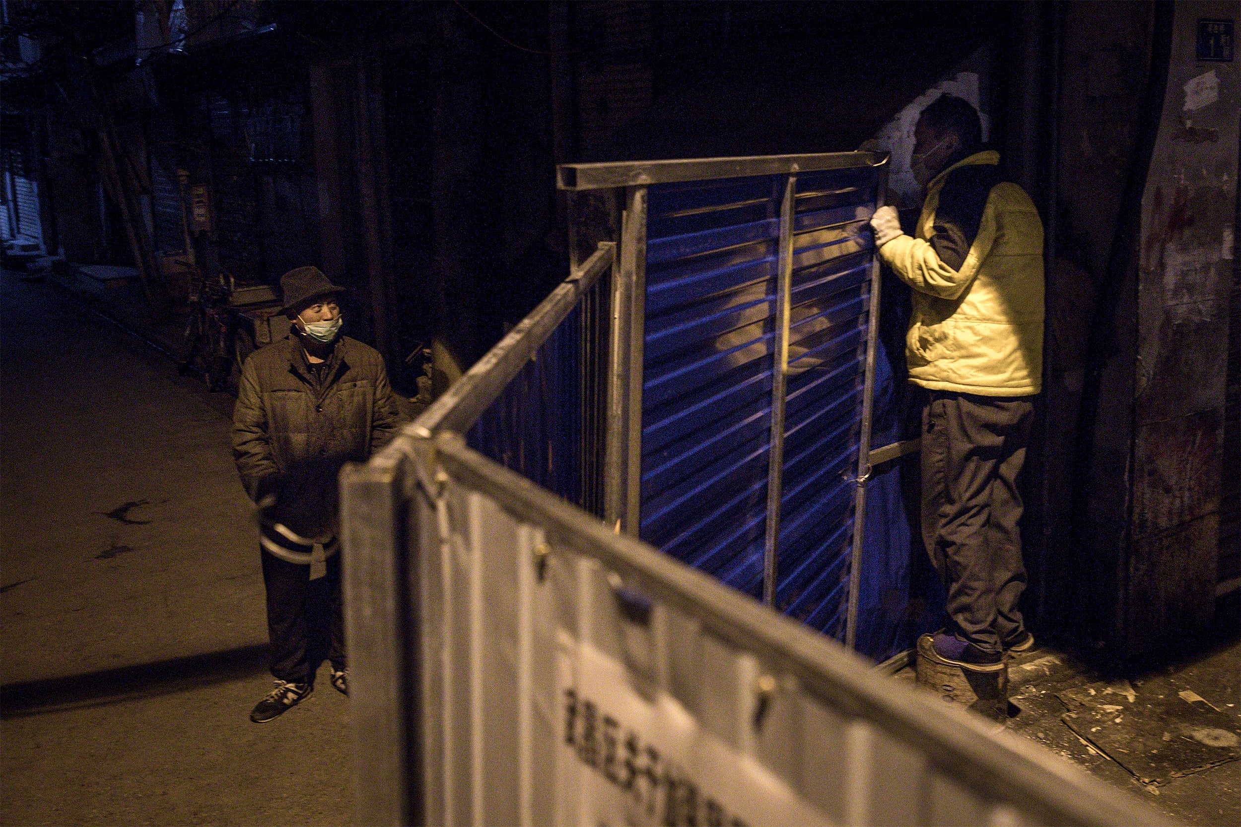 Image: Two men speak over a makeshift barricade to control the entry and exit into a residential area in Wuhan on March 4, 2020.